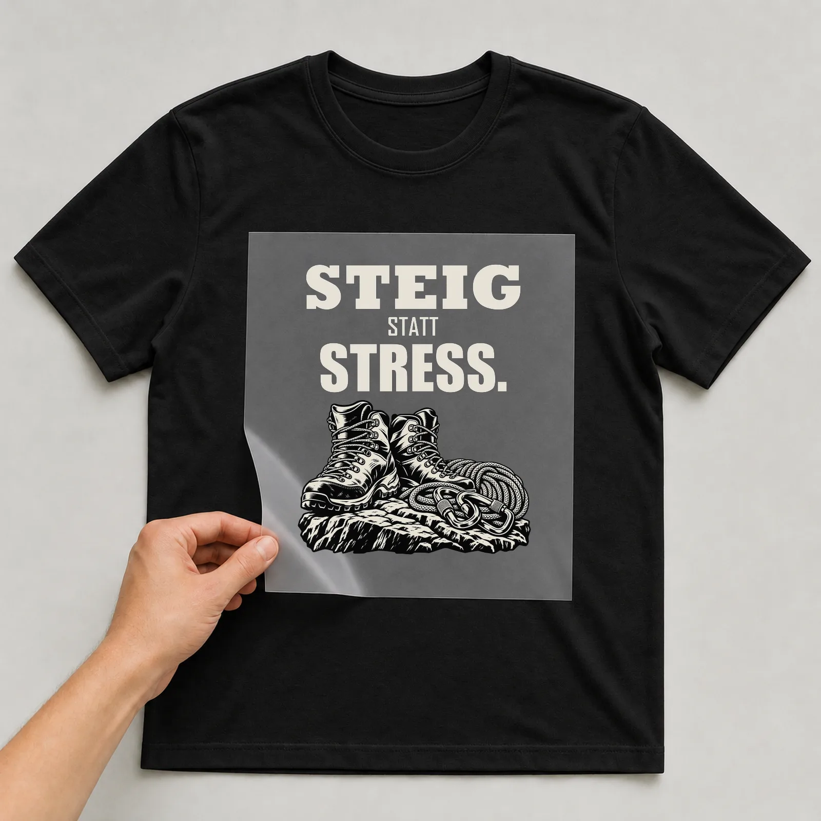 Bügelbild „Steig statt Stress“ auf schwarzem T-Shirt, Folie wird aufgelegt