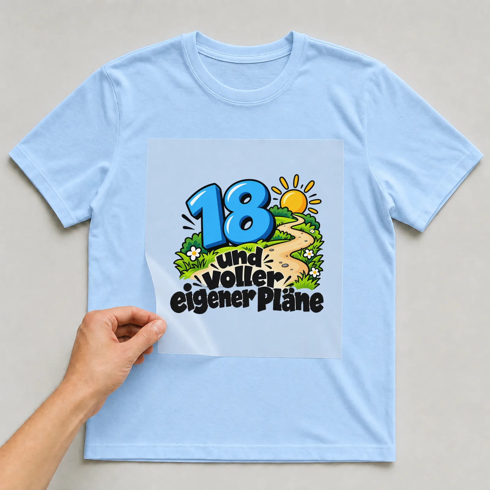 Bügelbild „18 und voller eigener Pläne“ auf hellblauem T-Shirt, Folie wird aufgelegt