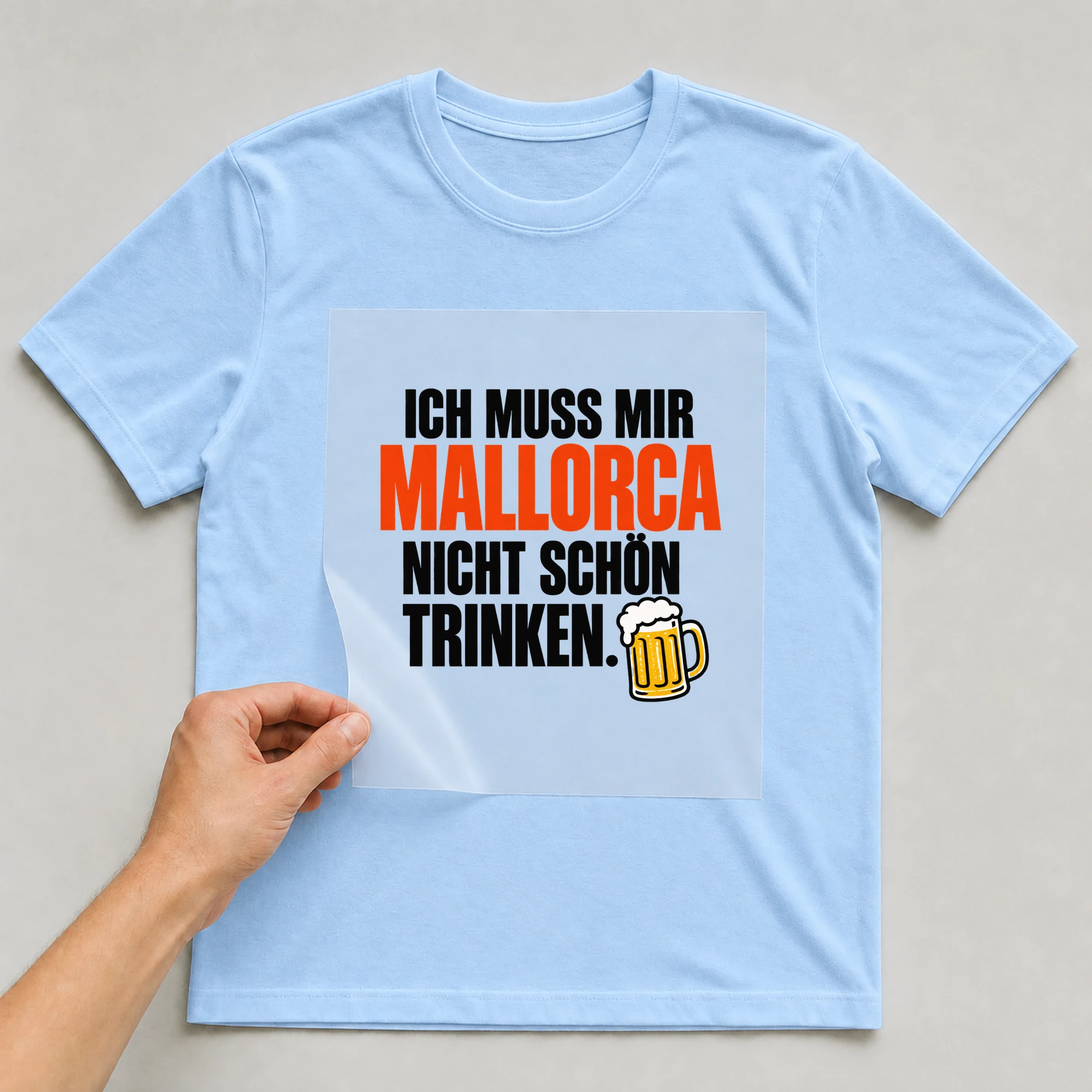 Bügelbild „Ich muss mir Mallorca nicht schön trinken.“ auf babyblauem T-Shirt, Folie wird aufgelegt