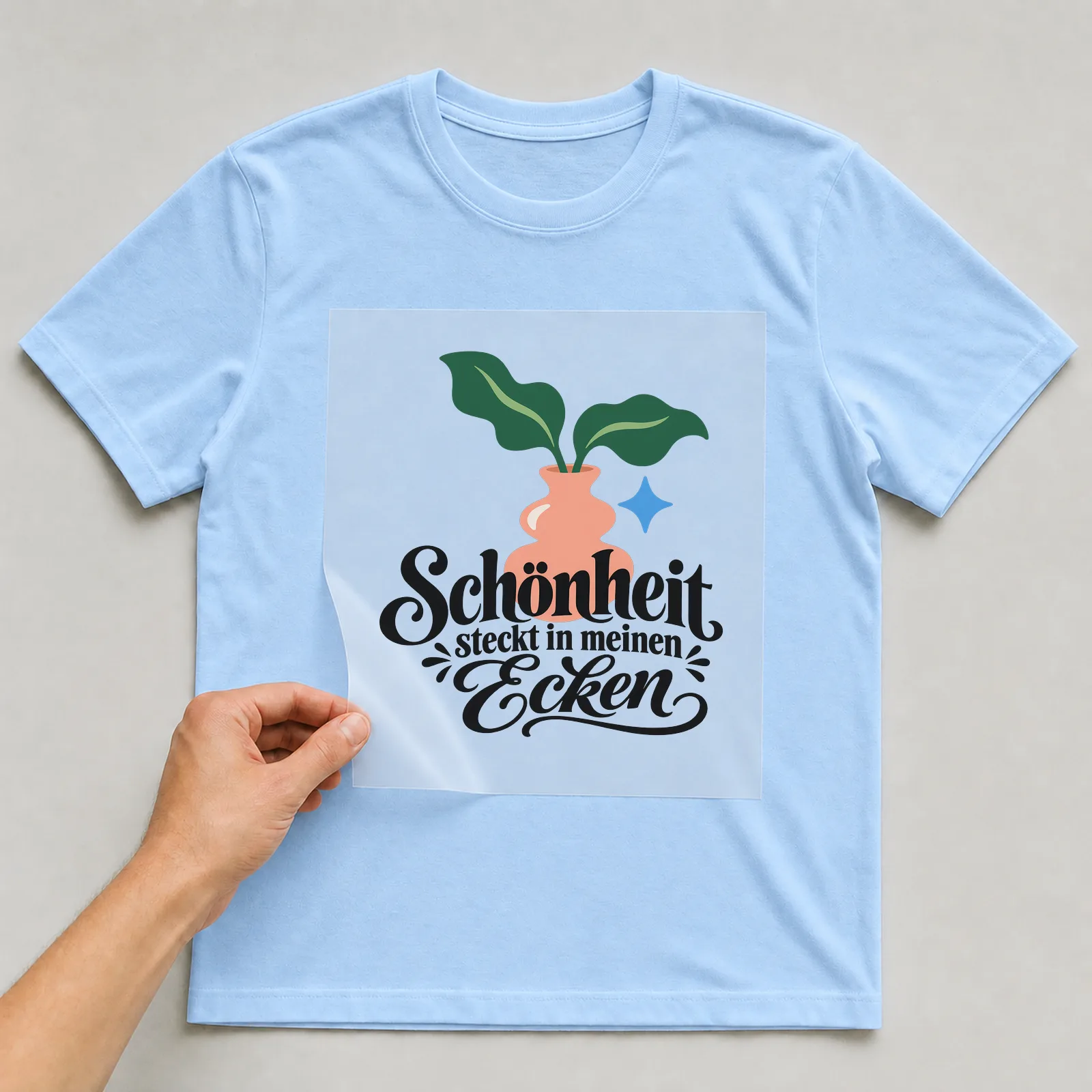 Bügelbild „Schönheit steckt in meinen Ecken“ auf hellblauem T-Shirt, Folie wird aufgelegt
