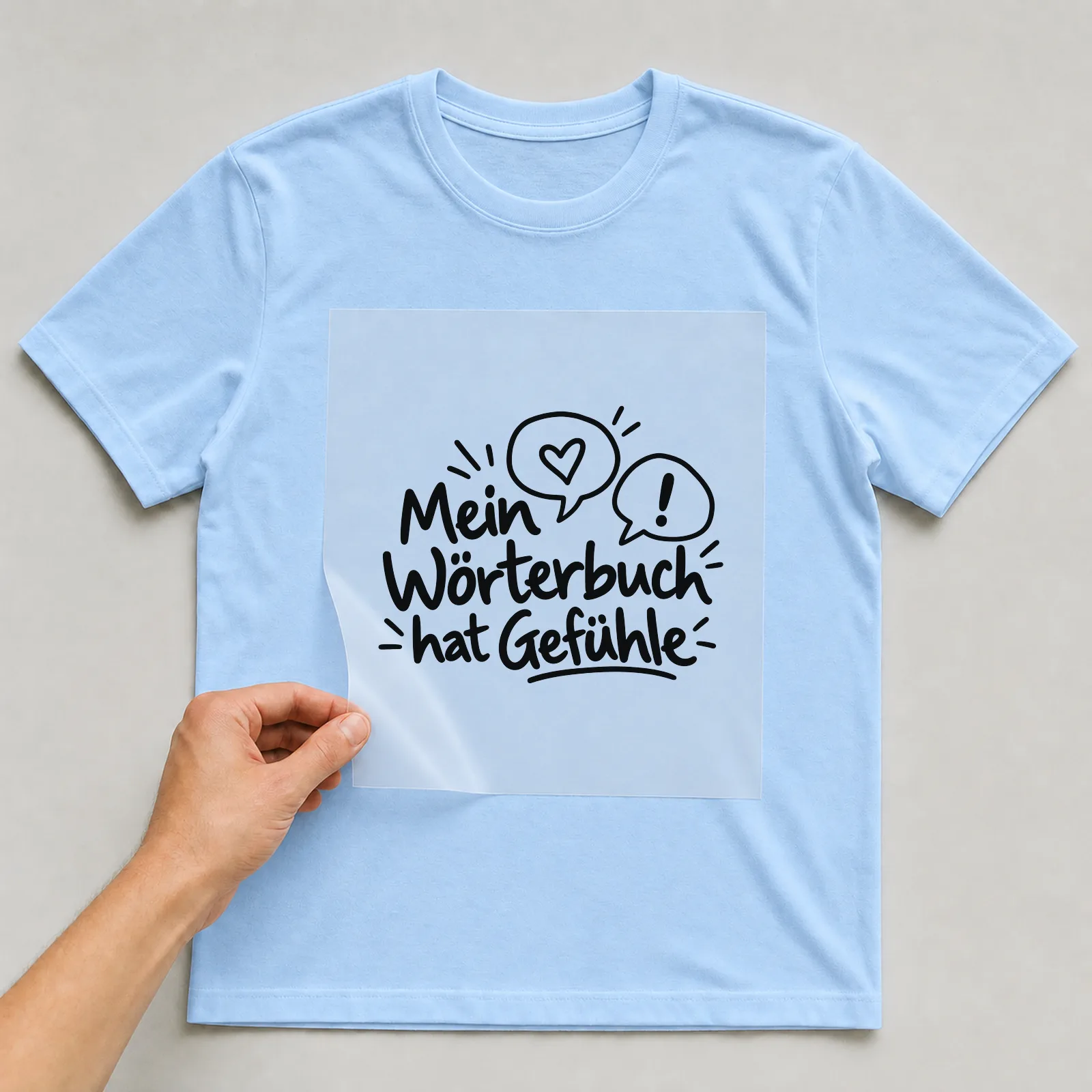 Bügelbild „Mein Wörterbuch hat Gefühle“ auf hellblauem T-Shirt, Folie wird aufgelegt