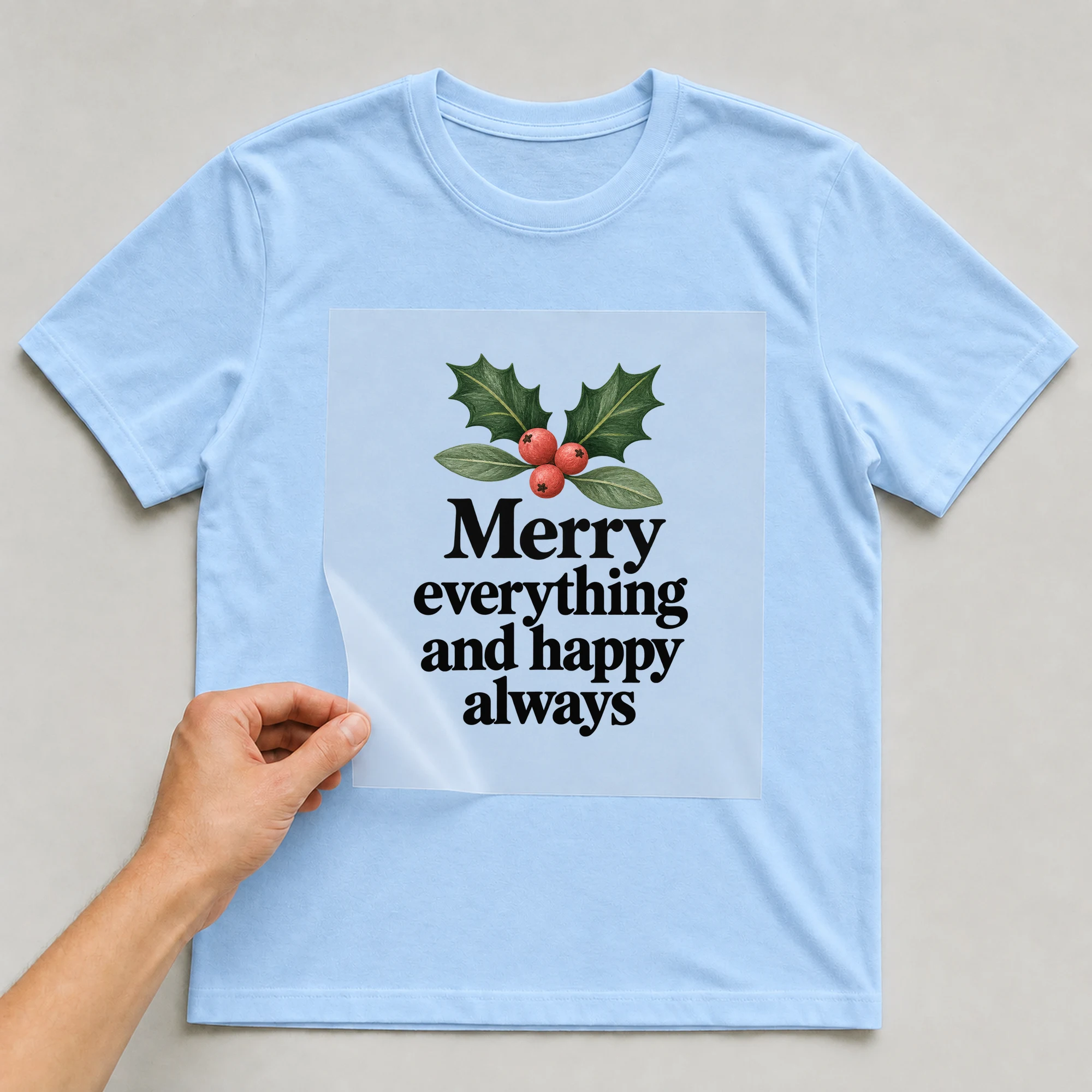 Bügelbild „Merry everything and happy always“ auf babyblauem T-Shirt, Folie wird aufgelegt