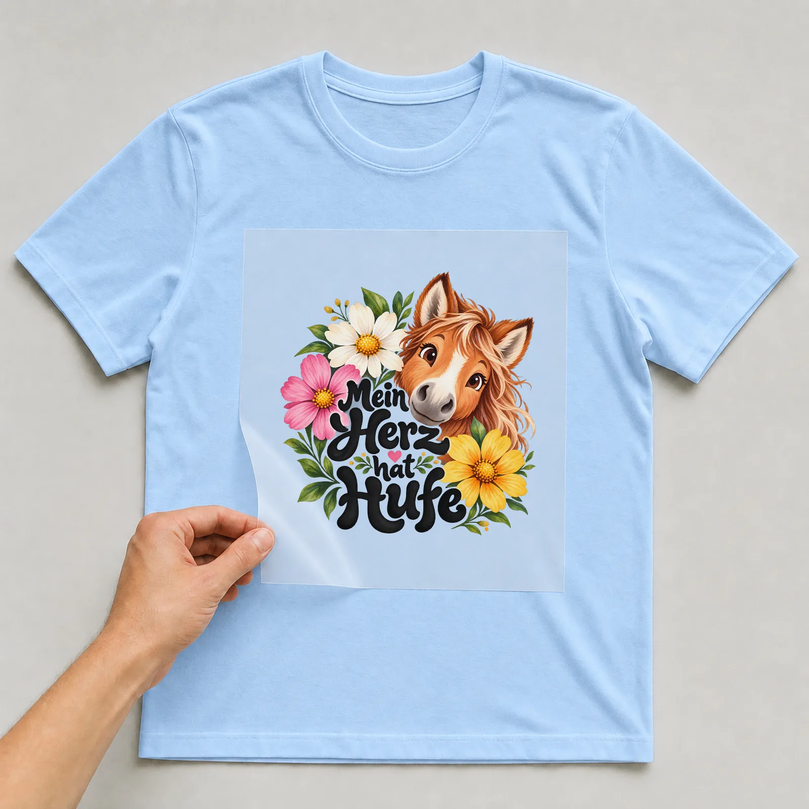 Bügelbild „Mein Herz hat Hufe“ auf hellblauem T-Shirt, Folie wird aufgelegt