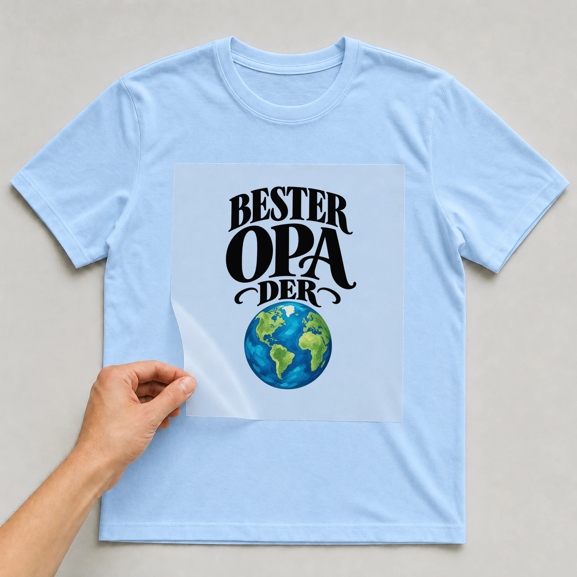 Bügelbild „Bester Opa Der Welt“ auf babyblauem T-Shirt, Folie wird aufgelegt