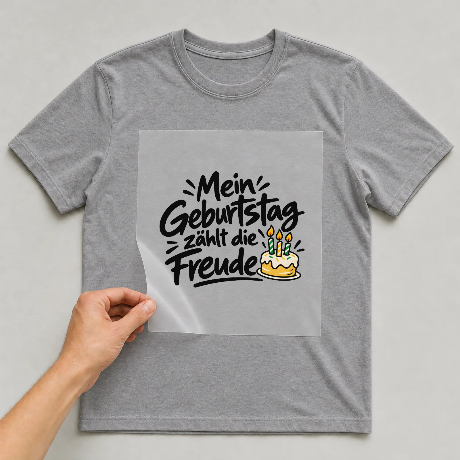 Bügelbild „Mein Geburtstag zählt die Freude“ auf grauem T-Shirt, Folie wird aufgelegt