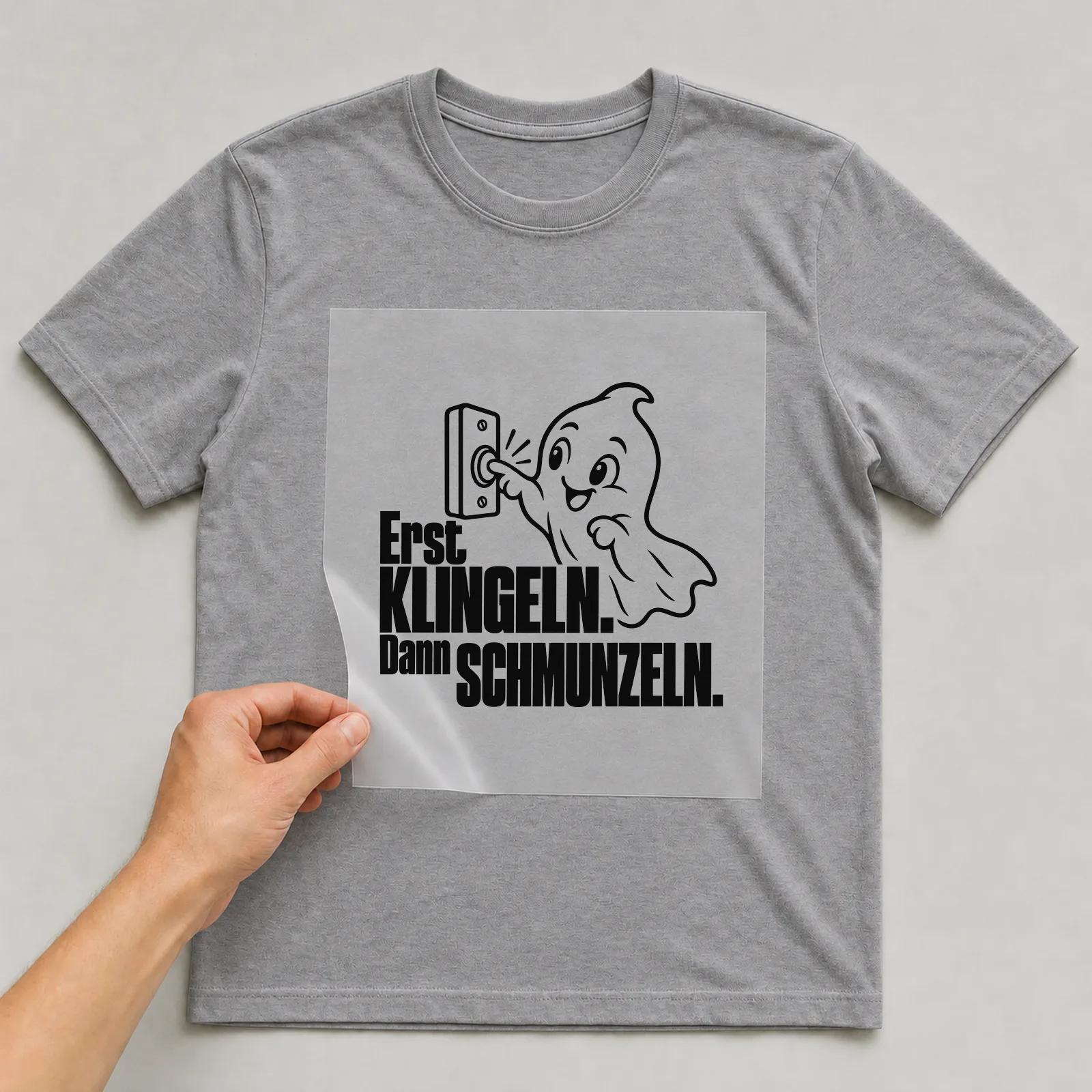 Bügelbild „Erst klingeln. Dann schmunzeln.“ auf grauem T-Shirt, Folie wird aufgelegt