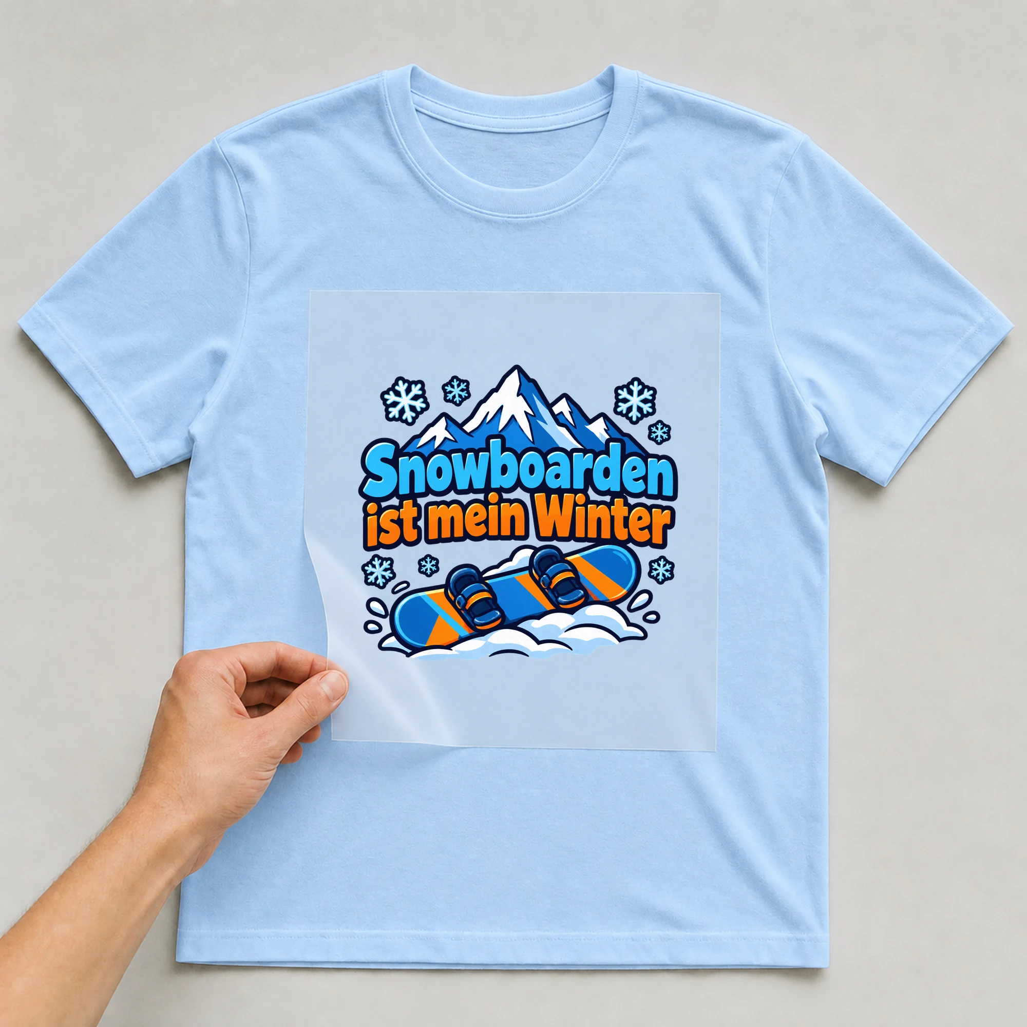 Bügelbild „Snowboarden ist mein Winter“ auf babyblauem T-Shirt, Folie wird aufgelegt