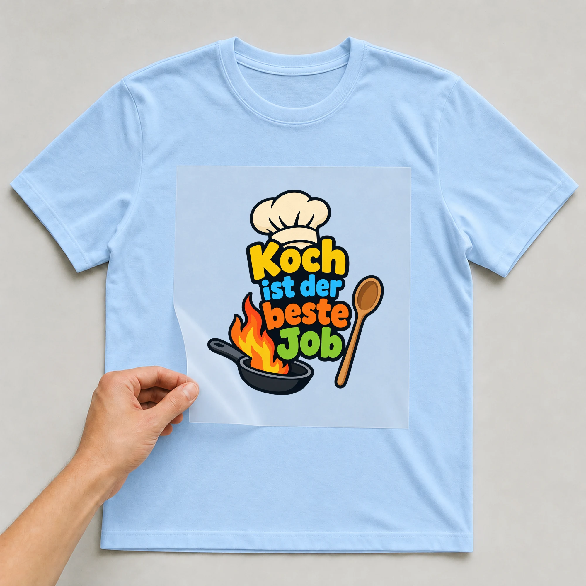 Bügelbild „Koch ist der beste Job“ auf babyblauem T-Shirt, Folie wird aufgelegt