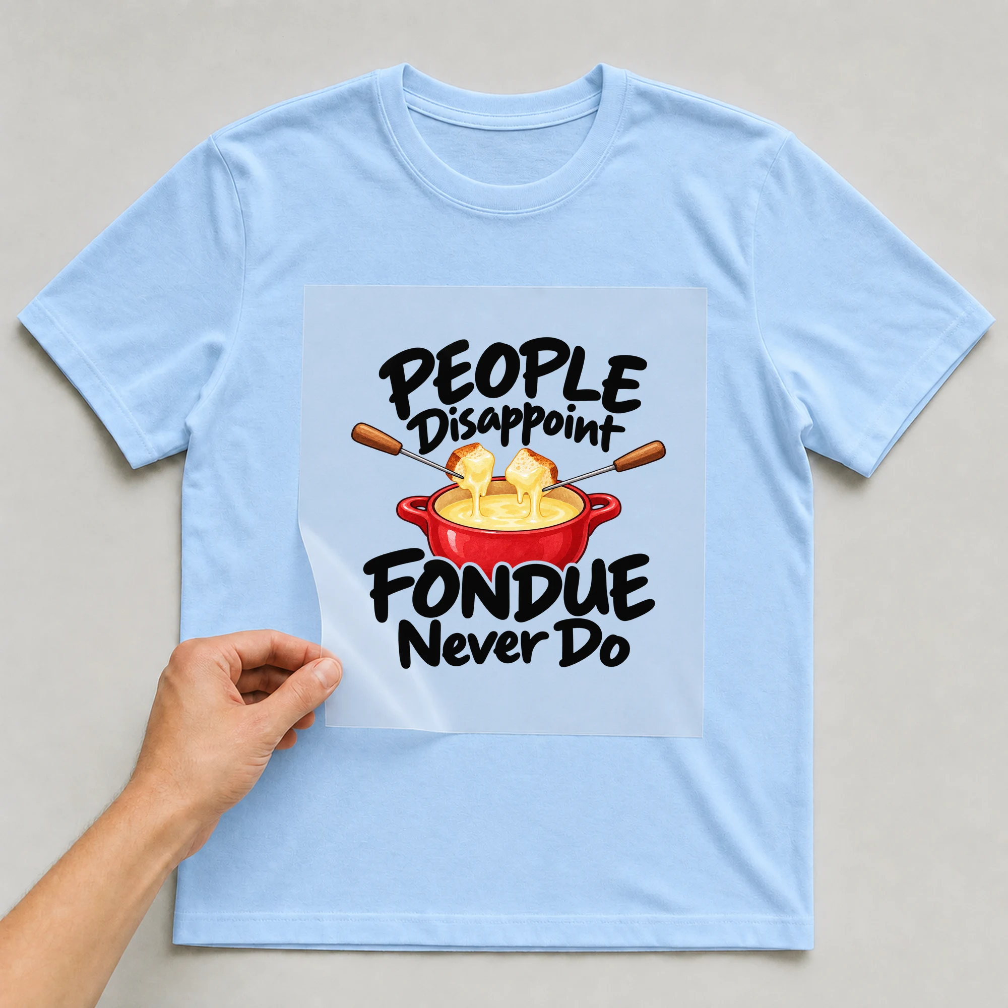 Bügelbild „People Disappoint Fondue Never Do“ auf babyblauem T-Shirt, Folie wird aufgelegt
