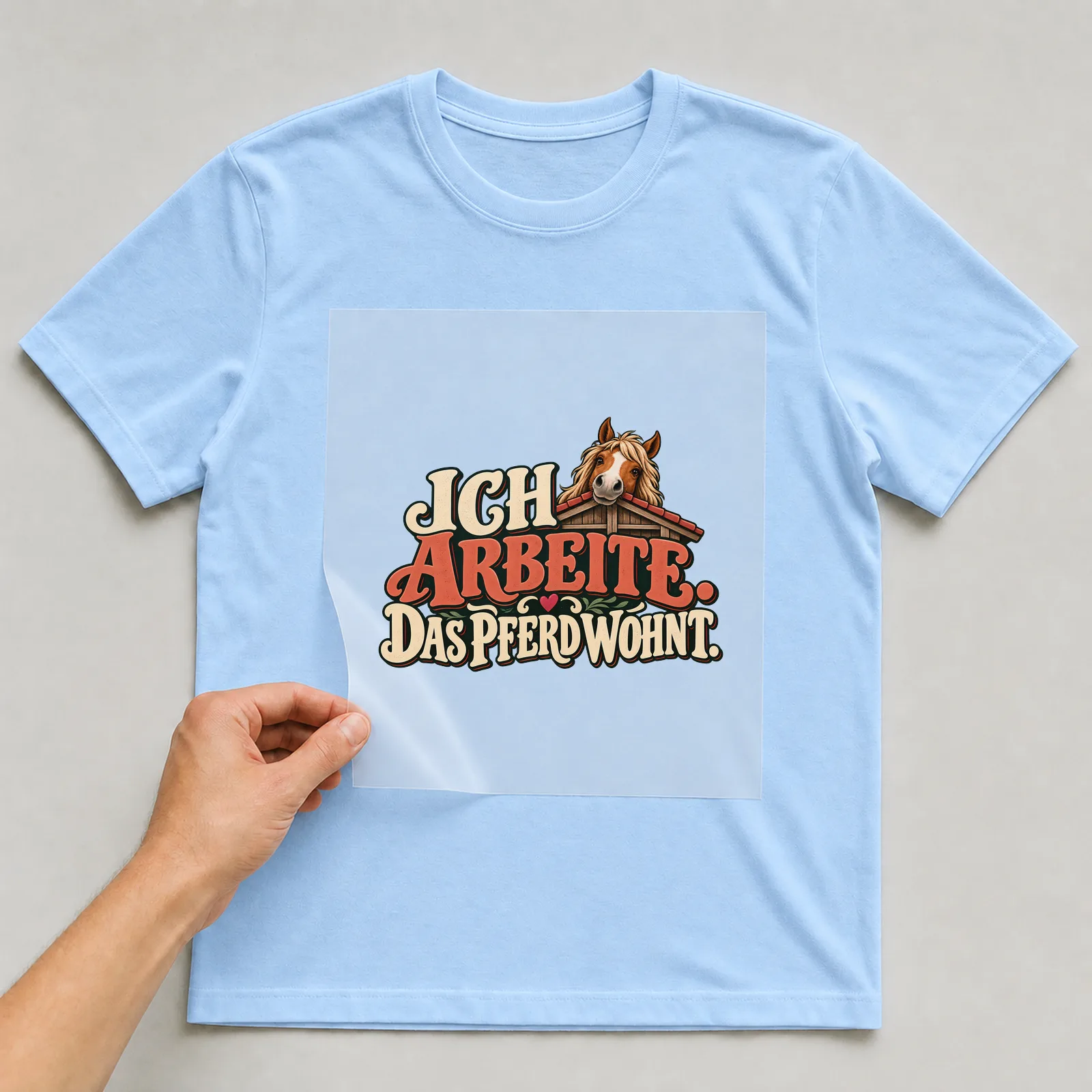 Bügelbild „Ich arbeite. Das Pferd wohnt.“ auf hellblauem T-Shirt, Folie wird aufgelegt