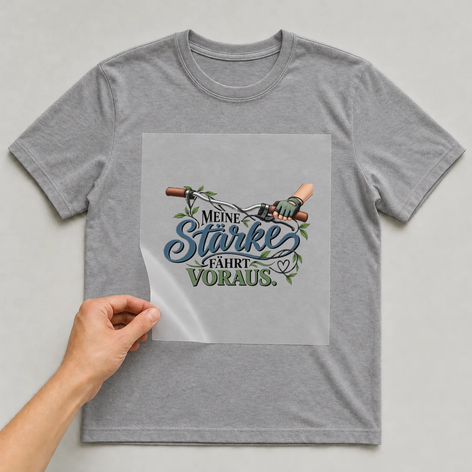 Bügelbild „Meine Stärke fährt voraus“ auf grauem T-Shirt, Folie wird aufgelegt