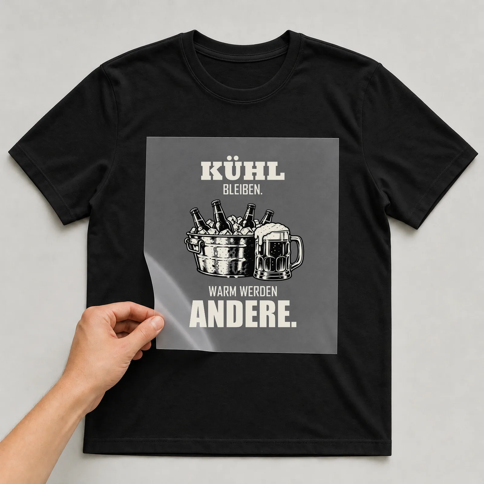 Bügelbild „Kühl bleiben. Warm werden andere.“ auf schwarzem T-Shirt, Folie wird aufgelegt