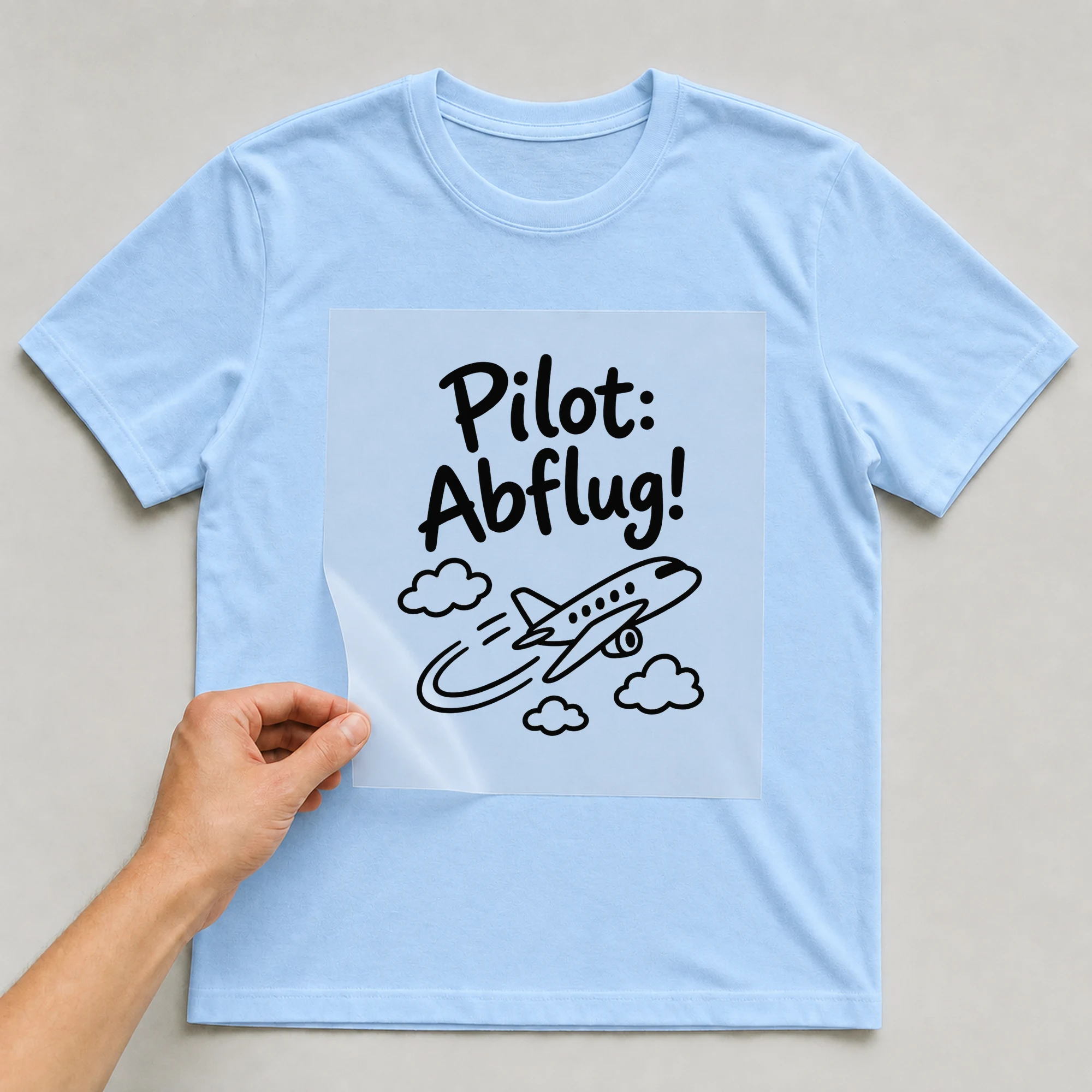 Bügelbild „Pilot: Abflug!“ auf babyblauem T-Shirt, Folie wird aufgelegt
