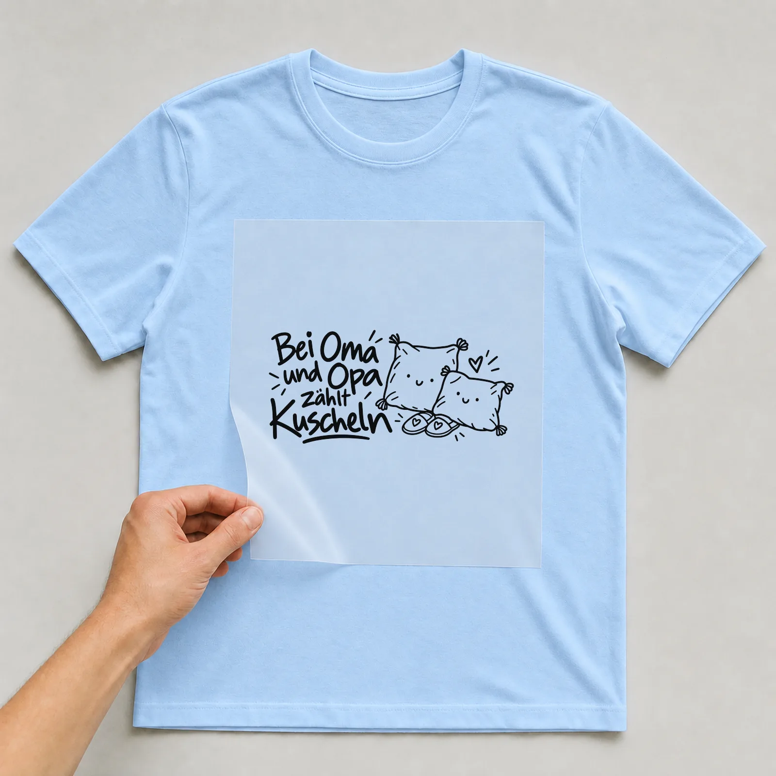 Bügelbild „Bei Oma und Opa zählt Kuscheln“ auf hellblauem T-Shirt, Folie wird aufgelegt
