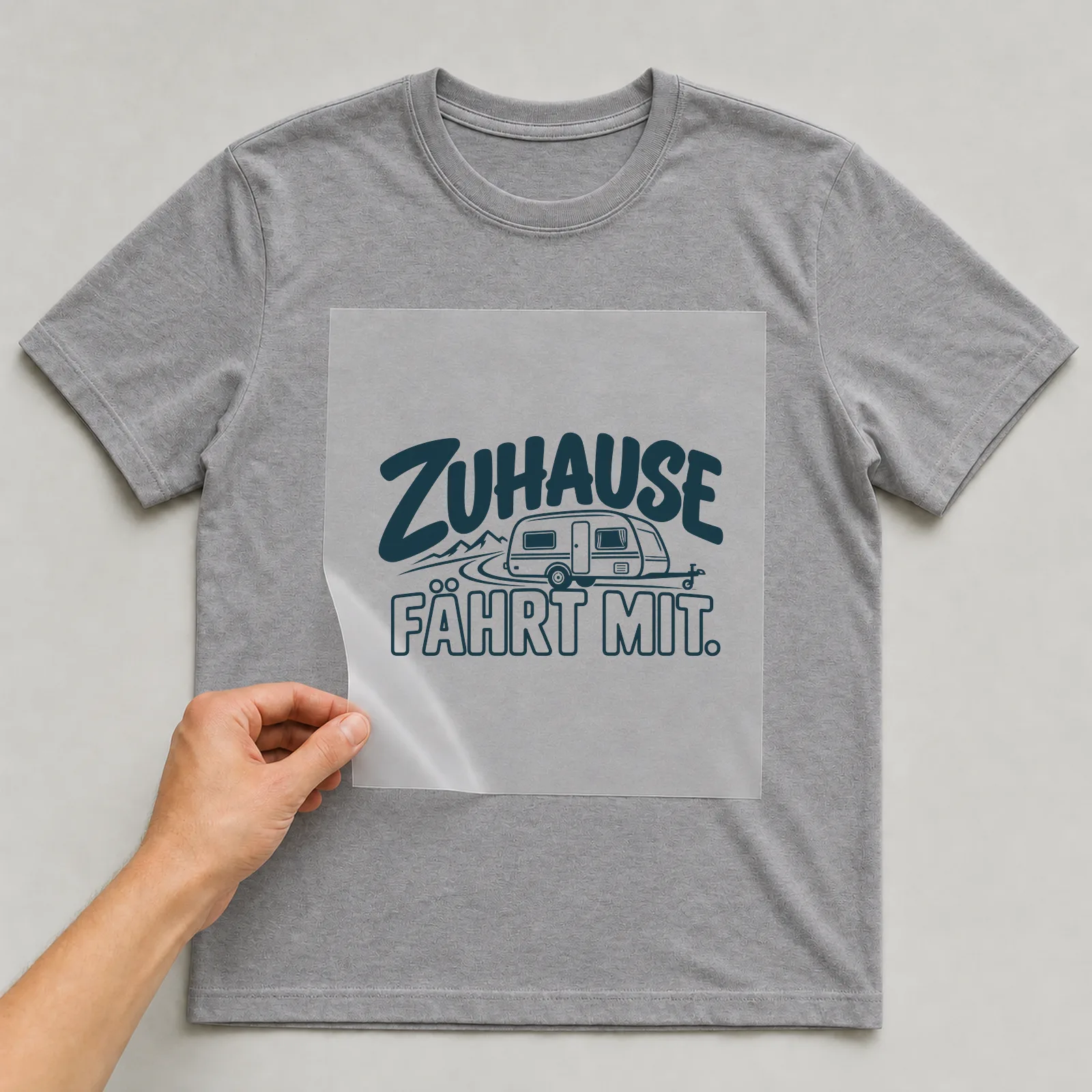 Bügelbild „Zuhause fährt mit“ auf grauem T-Shirt, Folie wird aufgelegt