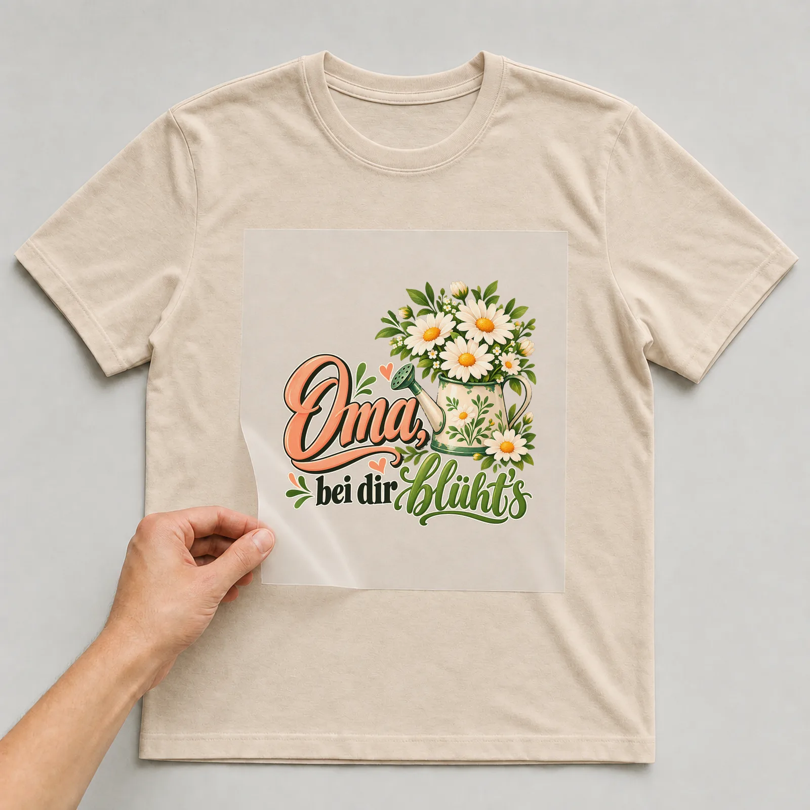 Bügelbild „Oma, bei dir blüht’s“ auf beigem T-Shirt, Folie wird aufgelegt