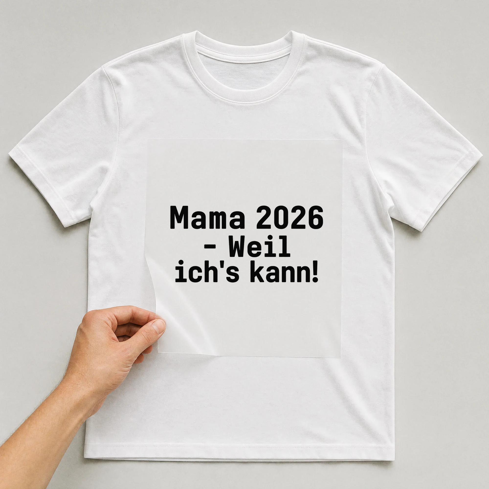 Bügelbild „Mama 2026 - weil ich's kann!“ auf weißem T-Shirt, Folie wird aufgelegt