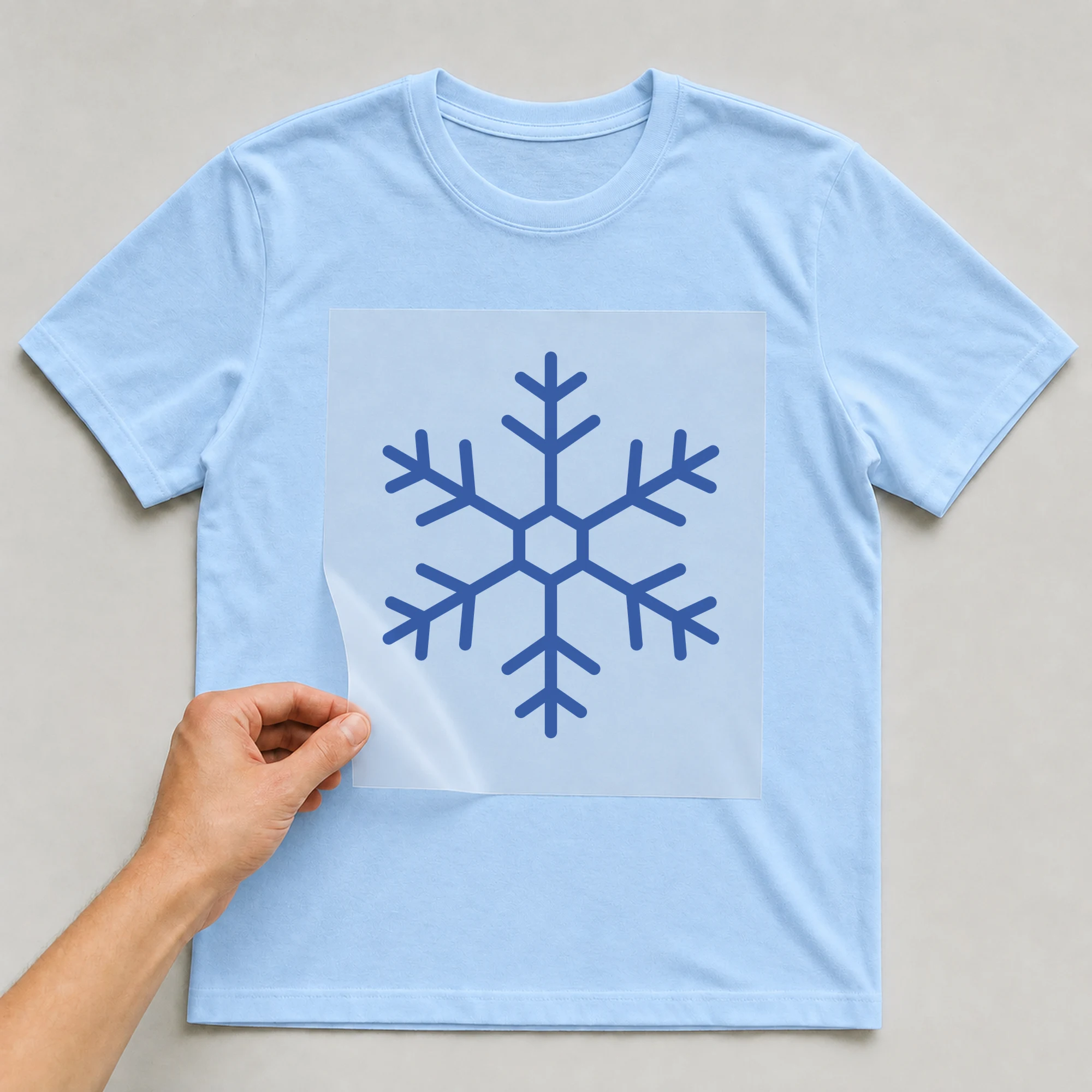 Bügelbild „Schneeflocke klein“ auf babyblauem T-Shirt, Folie wird aufgelegt