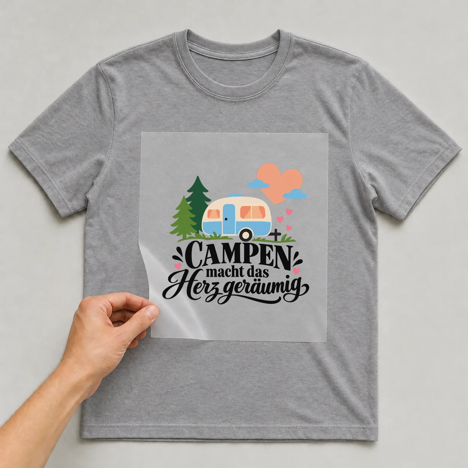 Bügelbild „CAMPEN macht das Herz geräumig“ auf grauem T-Shirt, Folie wird aufgelegt