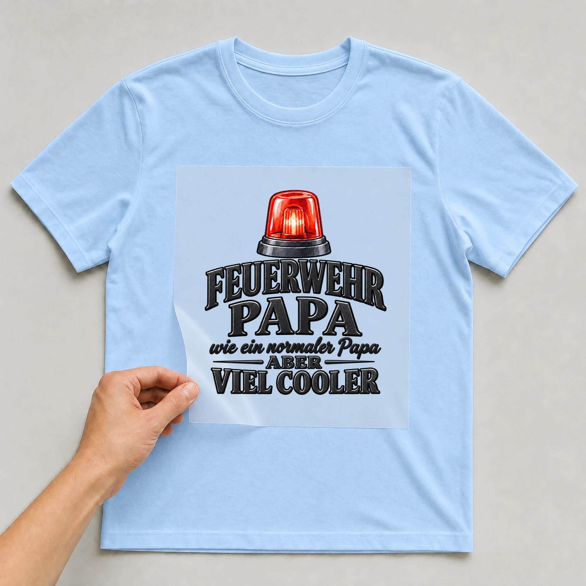 Bügelbild „Feuerwehr Papa wie ein normaler Papa aber viel cooler“ auf babyblauem T-Shirt, Folie wird aufgelegt