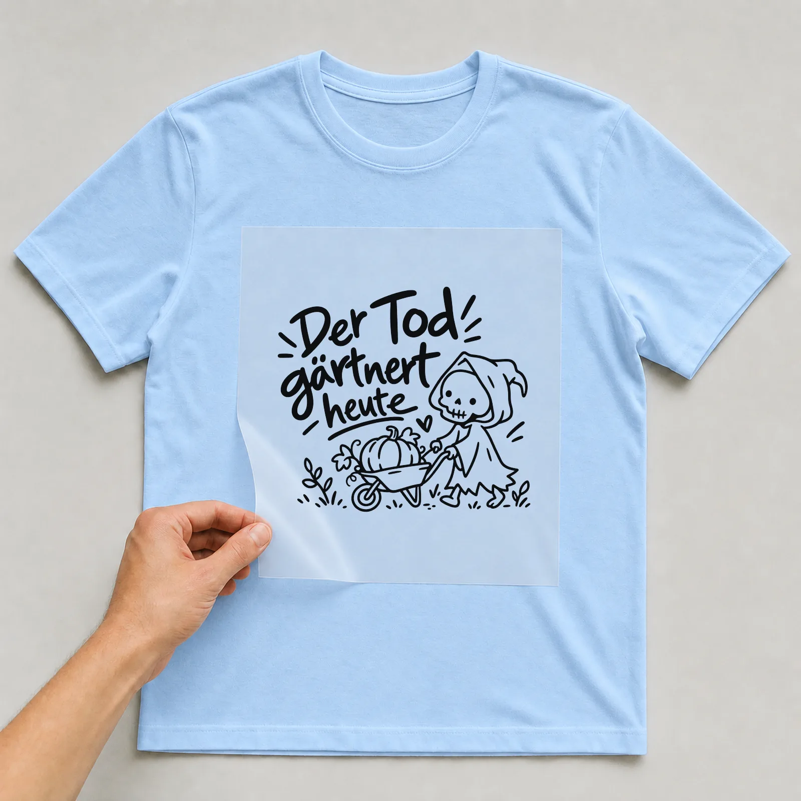 Bügelbild „Der Tod gärtnert heute“ auf hellblauem T-Shirt, Folie wird aufgelegt