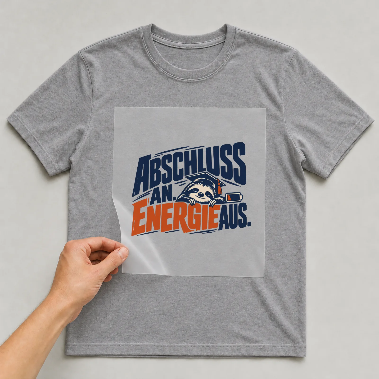 Bügelbild „Abschluss an. Energie aus.“ auf grauem T-Shirt, Folie wird aufgelegt