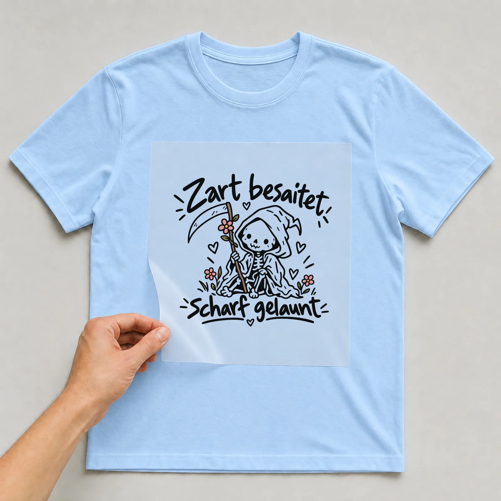 Bügelbild „Zart besaitet, scharf gelaunt“ auf hellblauem T-Shirt, Folie wird aufgelegt