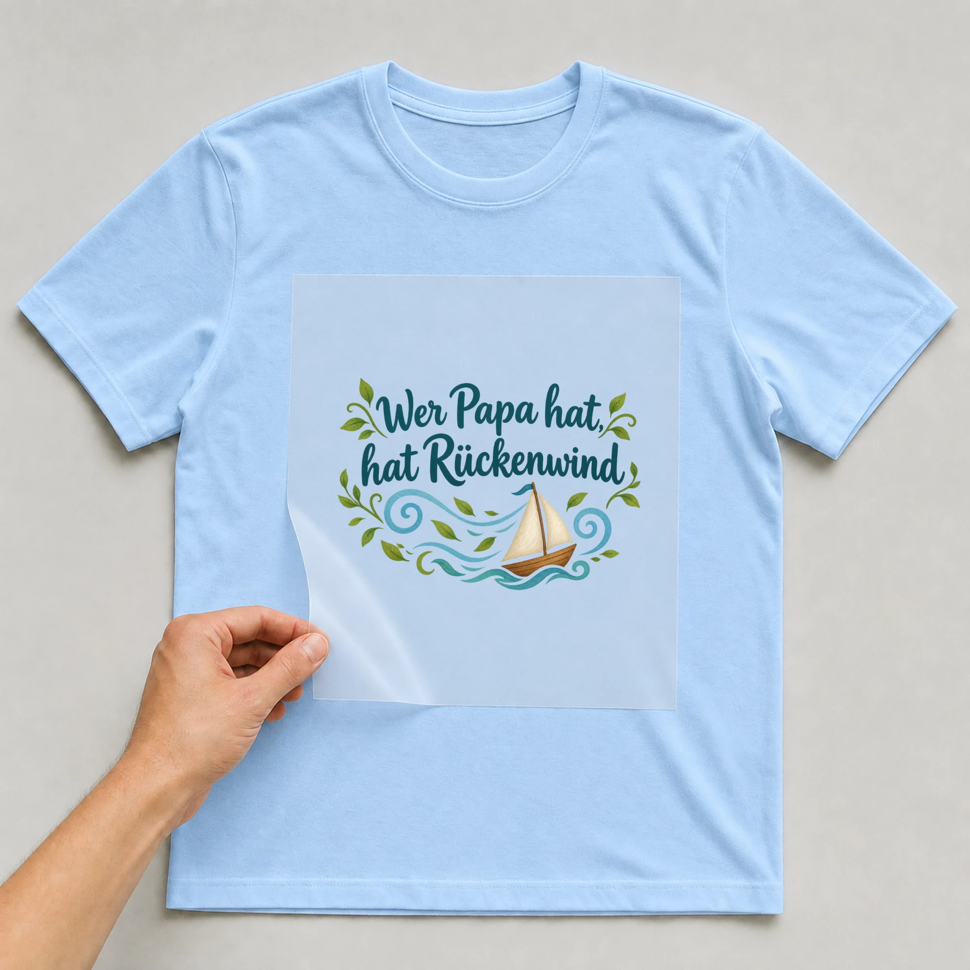 Bügelbild „Wer Papa hat, hat Rückenwind“ auf babyblauem T-Shirt, Folie wird aufgelegt