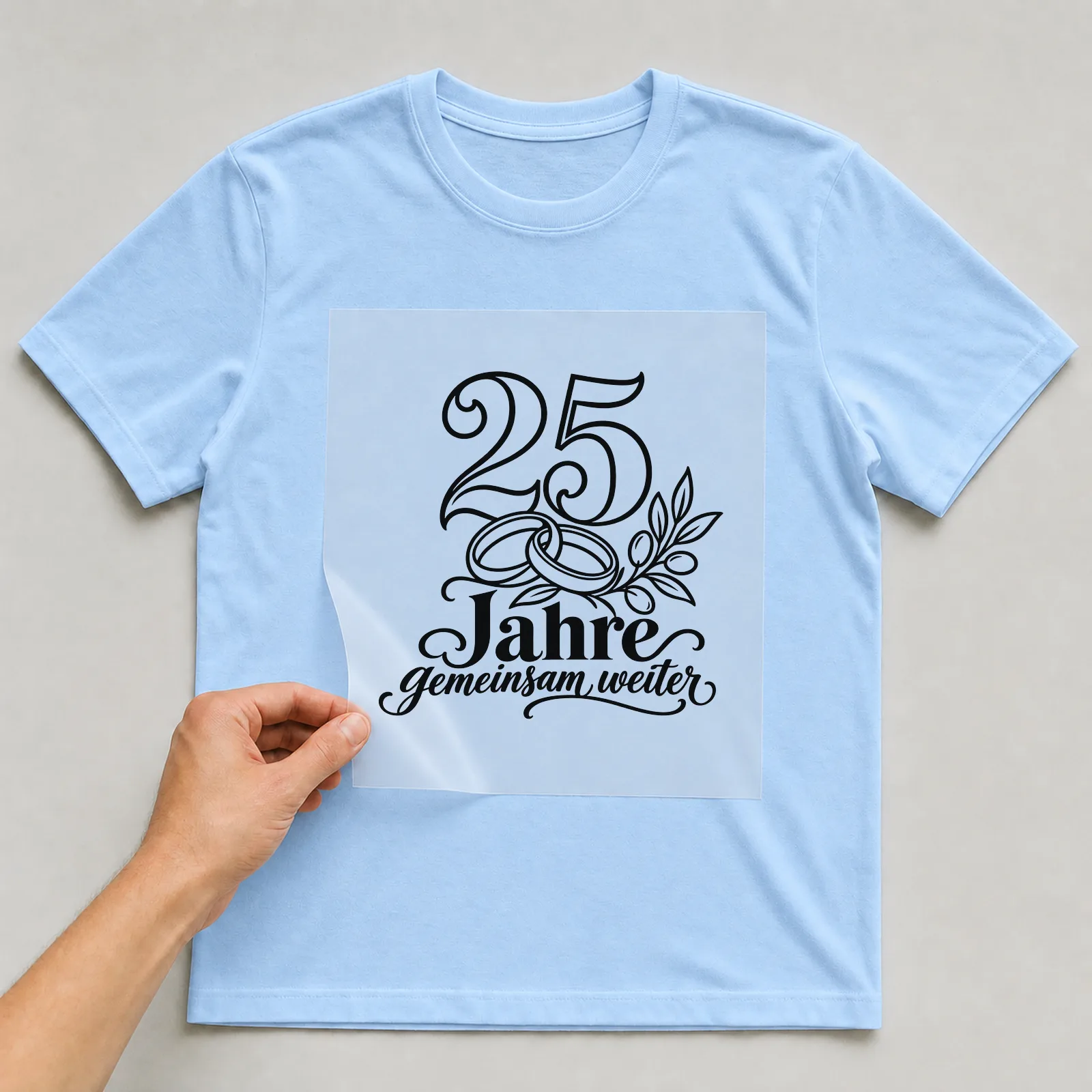Bügelbild „25 Jahre gemeinsam weiter“ auf hellblauem T-Shirt, Folie wird aufgelegt