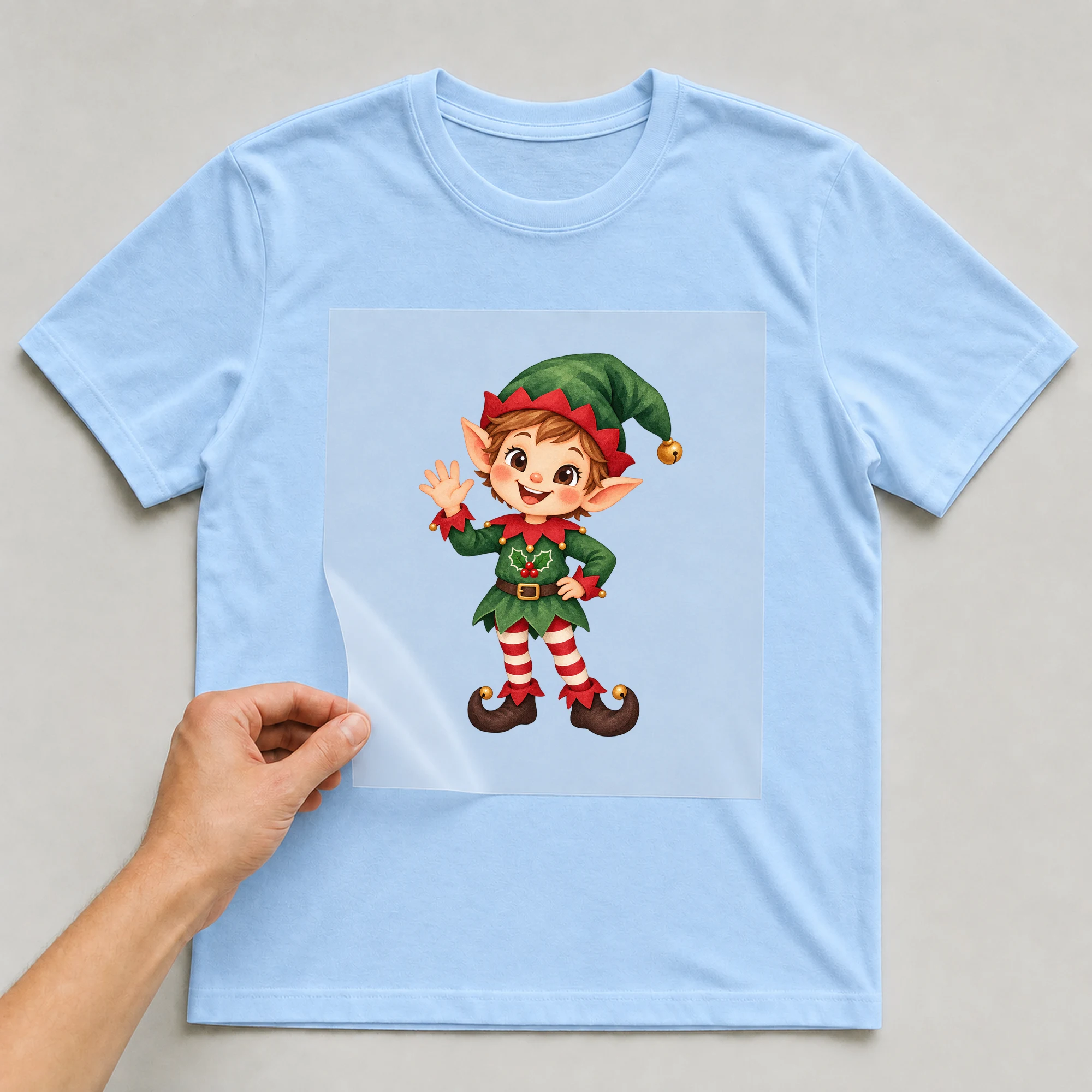 Bügelbild „Baby Elf Strumpf“ auf babyblauem T-Shirt, Folie wird aufgelegt
