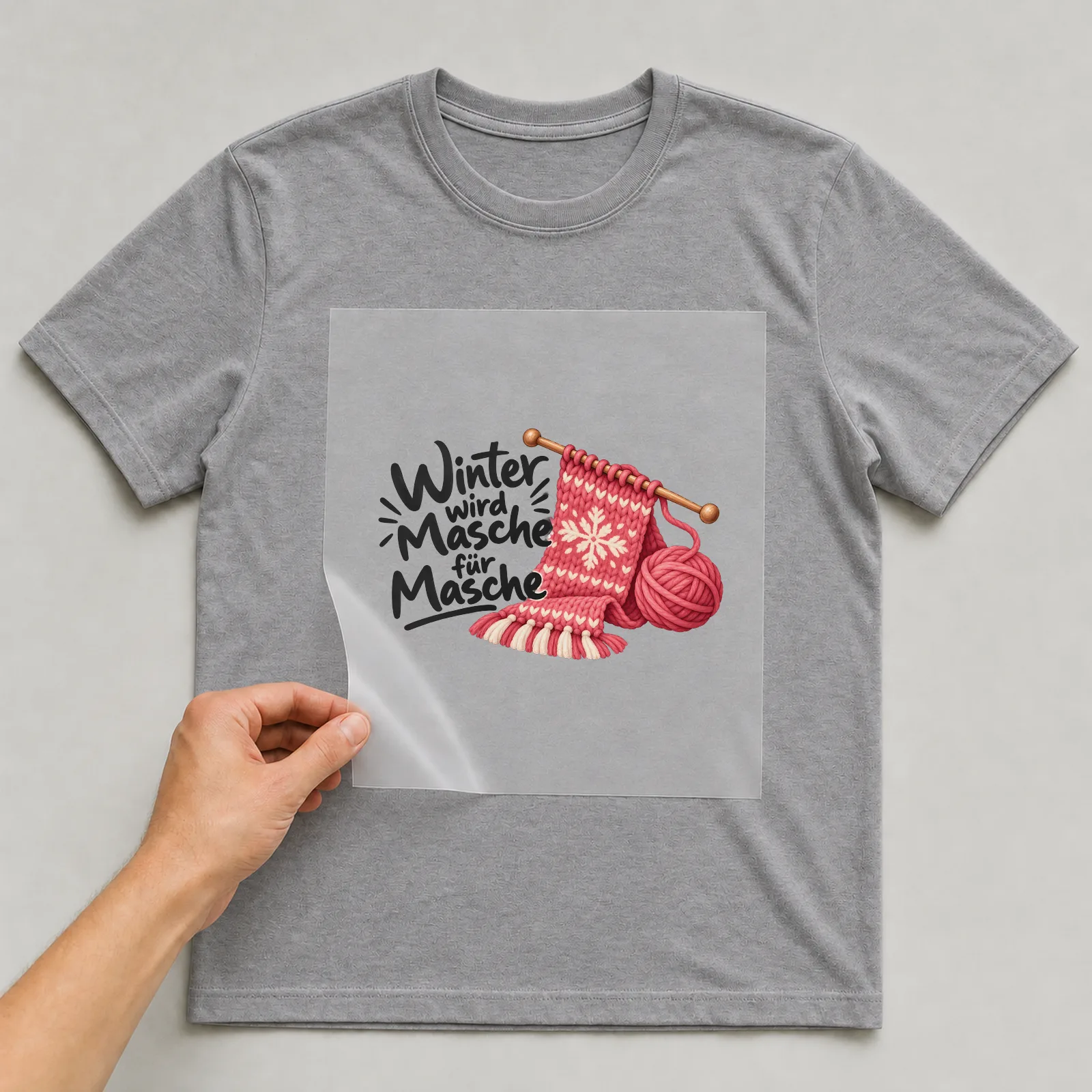 Bügelbild „Winter wird Masche für Masche“ auf grauem T-Shirt, Folie wird aufgelegt