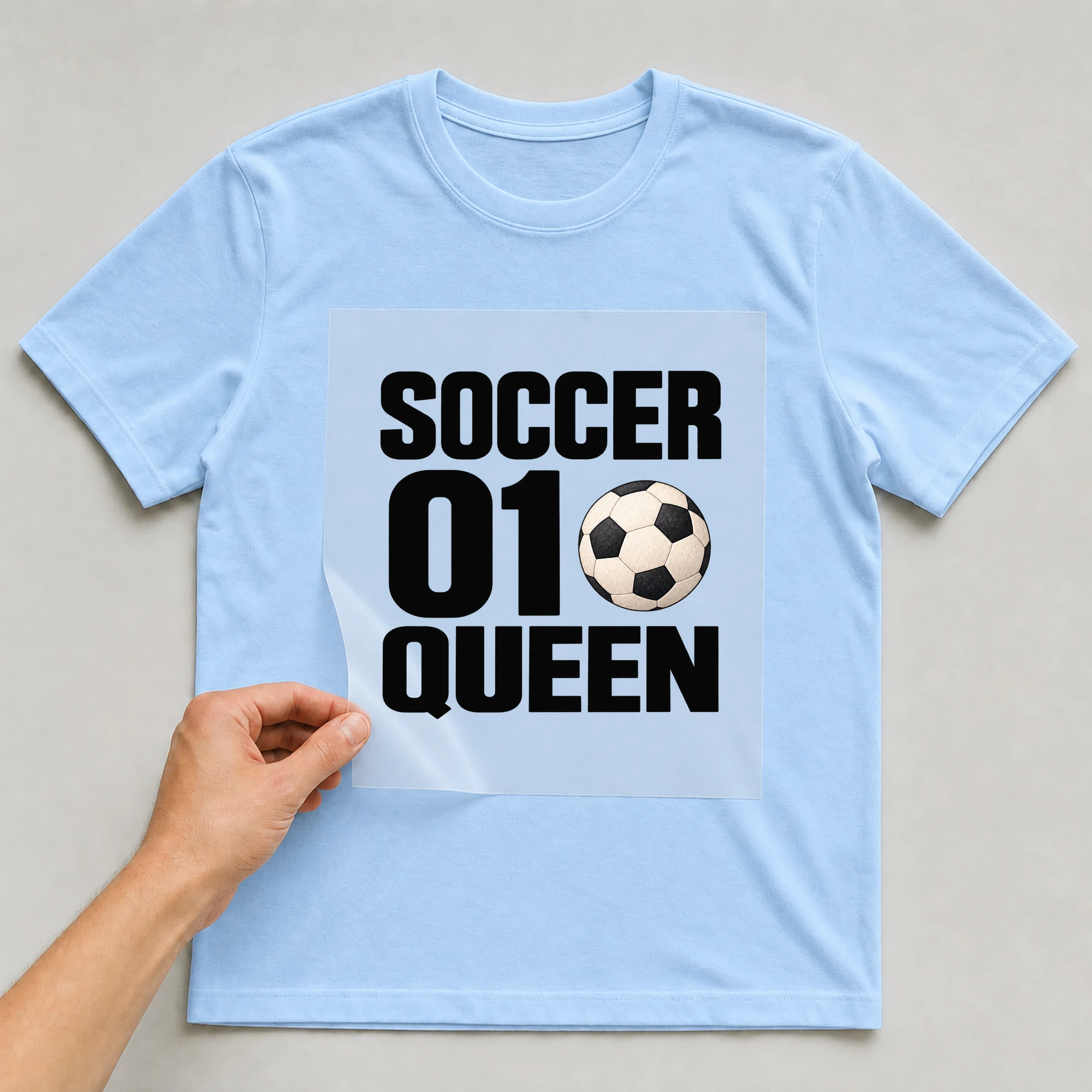 Bügelbild „Soccer 01 Queen“ auf babyblauem T-Shirt, Folie wird aufgelegt