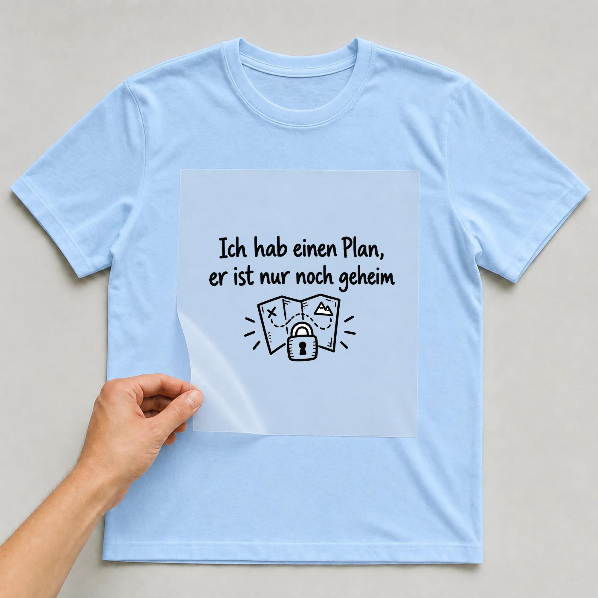 Bügelbild „Ich hab einen Plan, er ist nur noch geheim“ auf babyblauem T-Shirt, Folie wird aufgelegt