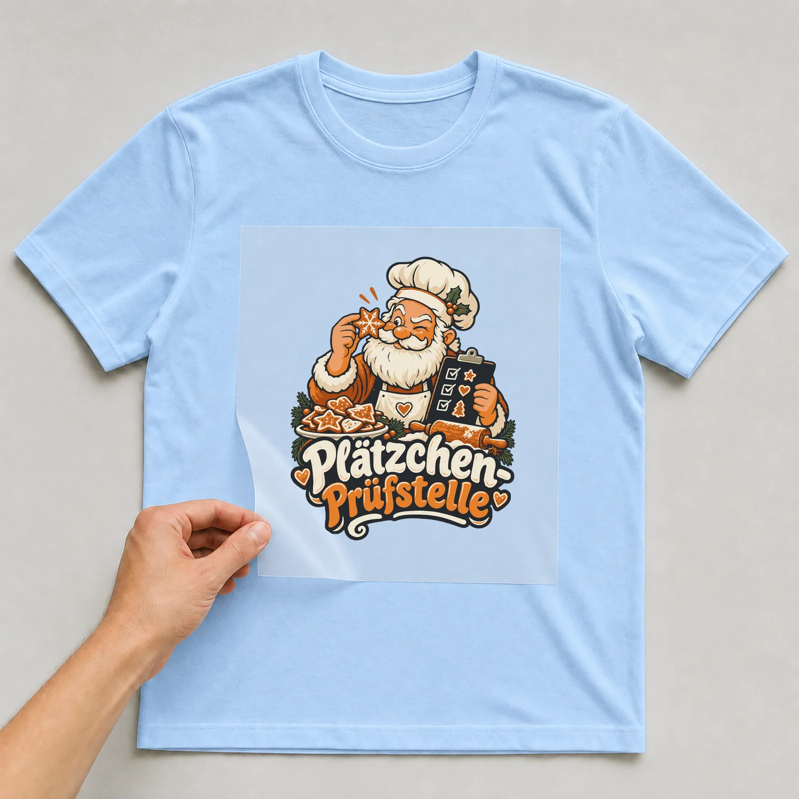 Bügelbild Plätzchen-Prüfstelle auf hellblauem T-Shirt, Folie wird aufgelegt