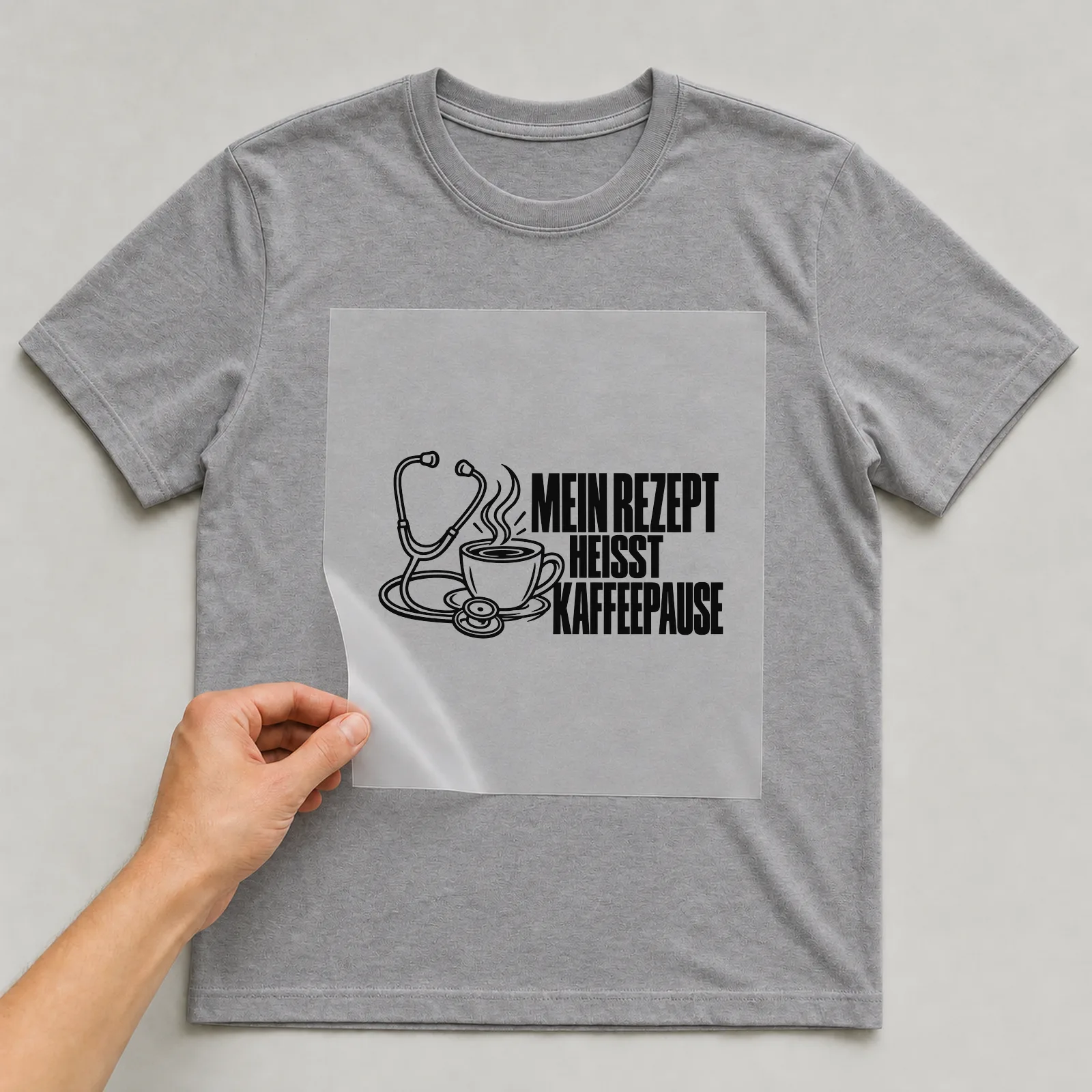 Bügelbild „Mein Rezept heißt Kaffeepause“ auf grauem T-Shirt, Folie wird aufgelegt