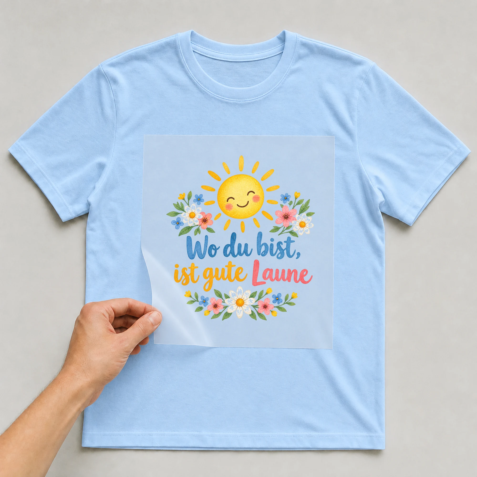 Bügelbild „Wo du bist, ist gute Laune“ auf babyblauem T-Shirt, Folie wird aufgelegt