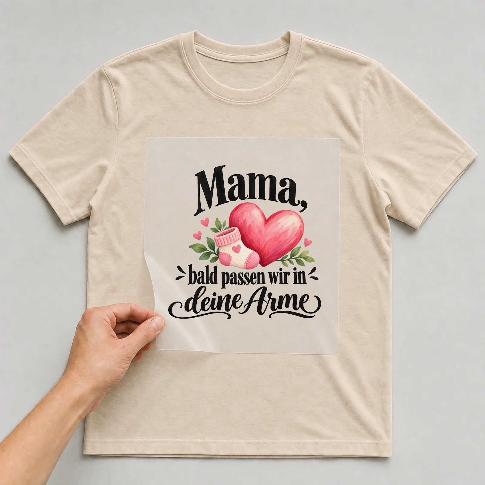 Bügelbild „Mama, bald passen wir in deine Arme“ auf beigem T-Shirt, Folie wird aufgelegt