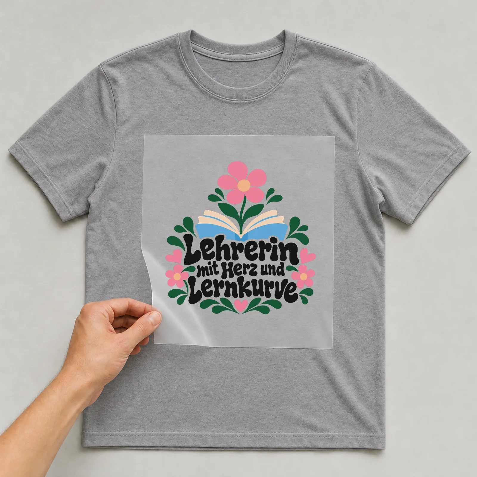 Bügelbild „Lehrerin mit Herz und Lernkurve“ auf grauem T-Shirt, Folie wird aufgelegt
