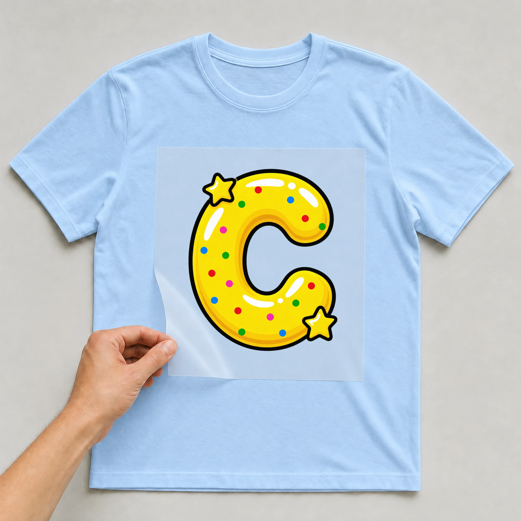 Bügelbild „Buchstabe C im Comic-Ballon-Stil“ auf babyblauem T-Shirt, Folie wird aufgelegt