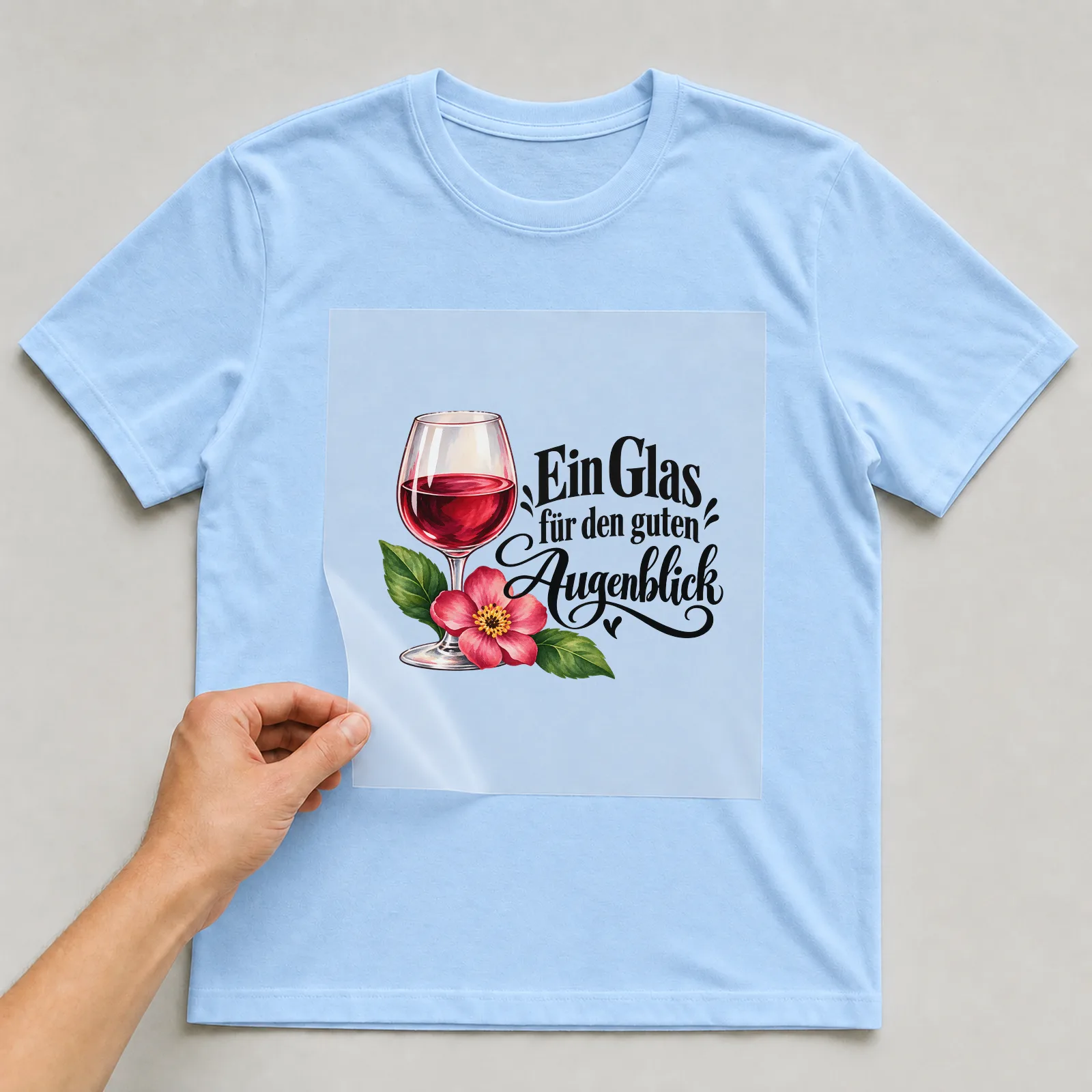 Bügelbild „Ein Glas für den guten Augenblick“ auf hellblauem T-Shirt, Folie wird aufgelegt