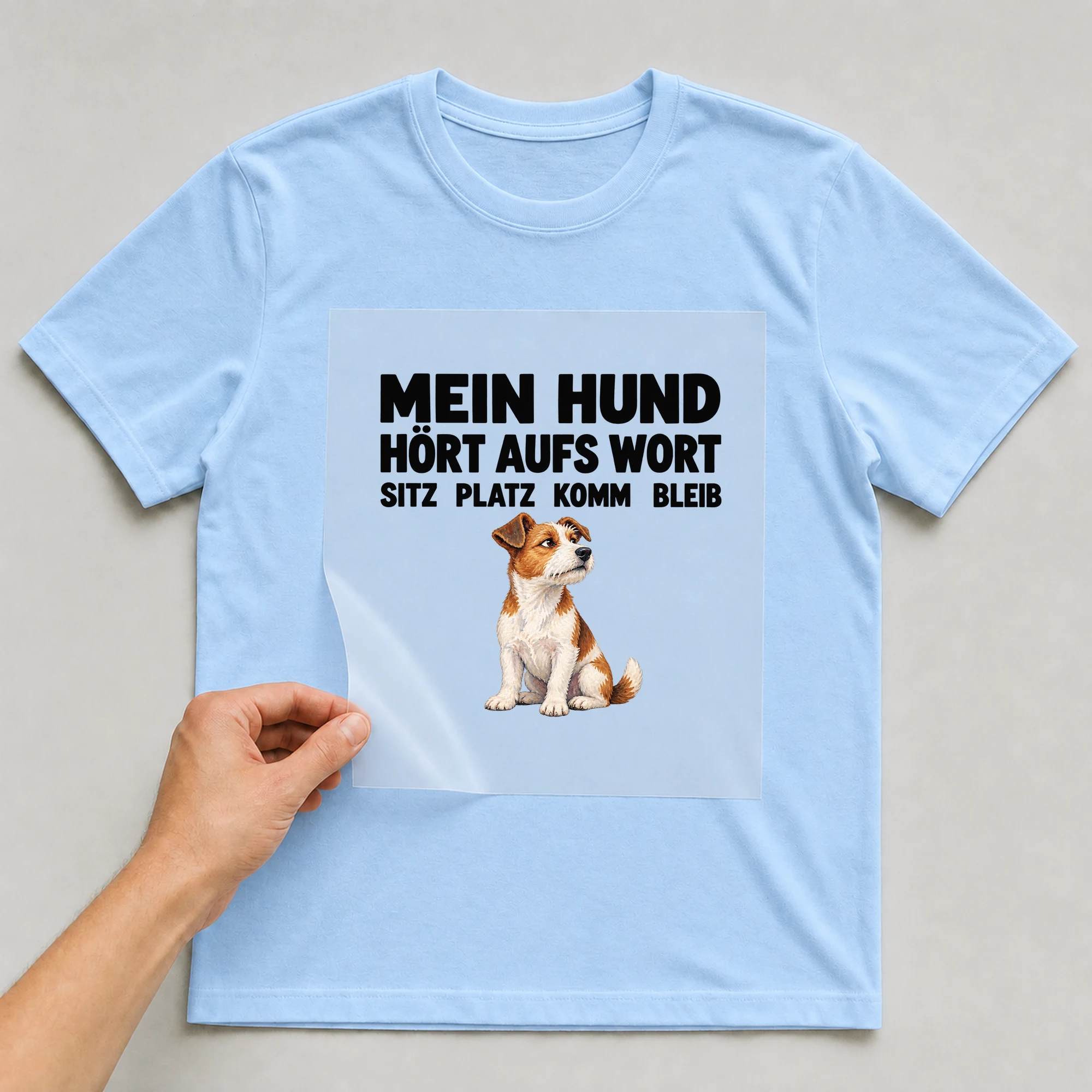 Bügelbild „Mein Hund Hört Aufs Wort Sitz Platz Komm Bleib“ auf babyblauem T-Shirt, Folie wird aufgelegt
