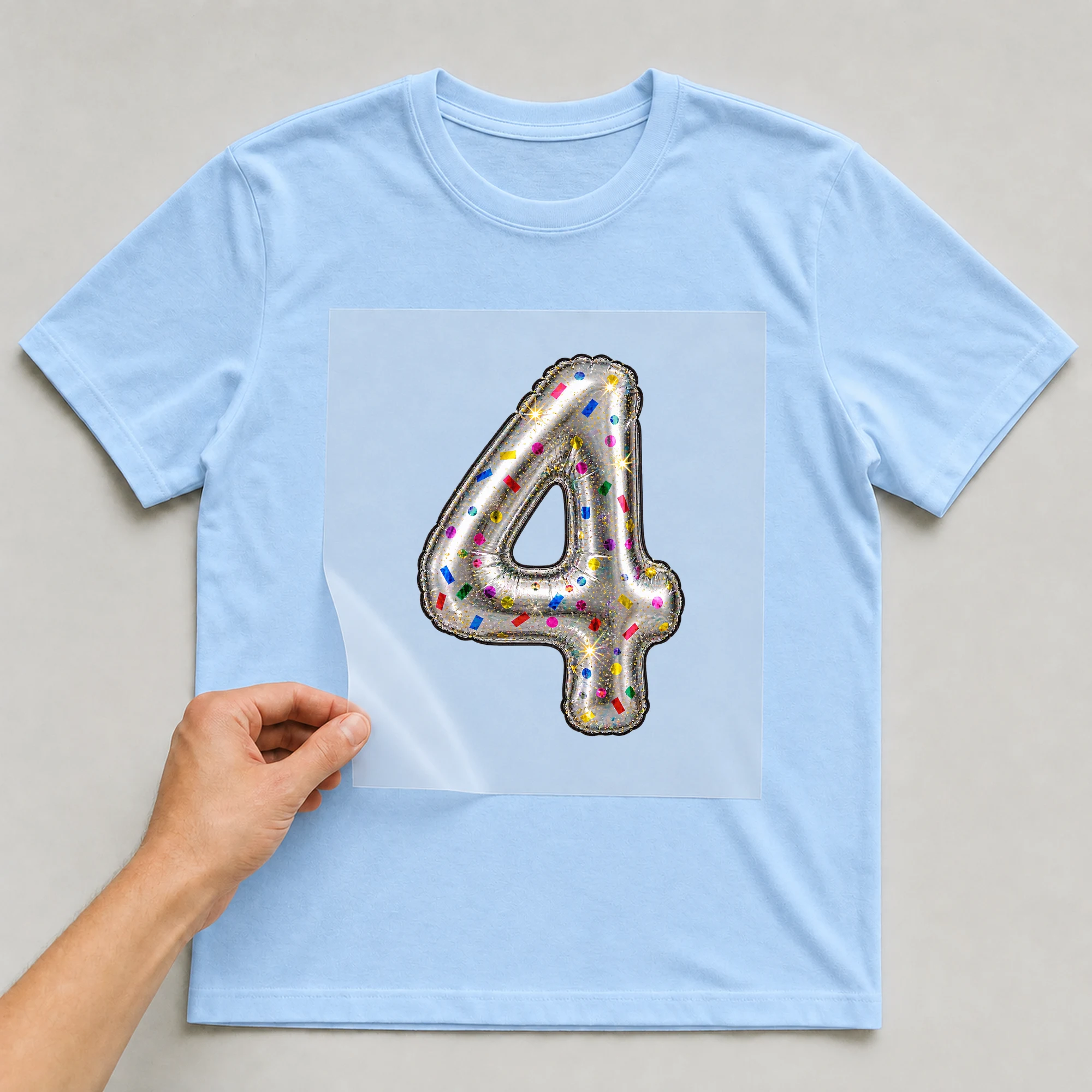 Bügelbild „Zahl 4 im Konfetti-Metallic-Look“ auf babyblauem T-Shirt, Folie wird aufgelegt