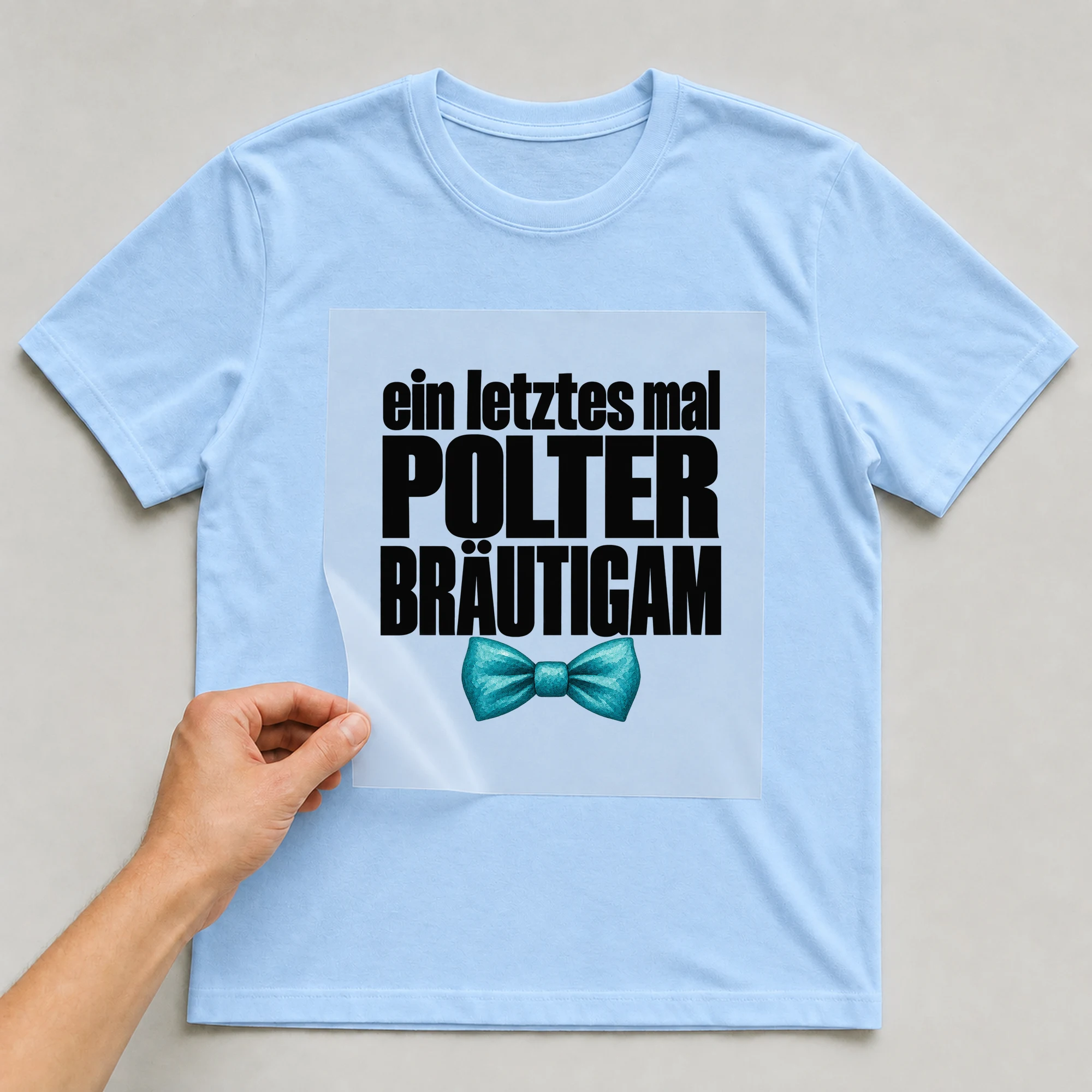 Bügelbild „Ein Letztes Mal Polter Bräutigam“ auf babyblauem T-Shirt, Folie wird aufgelegt