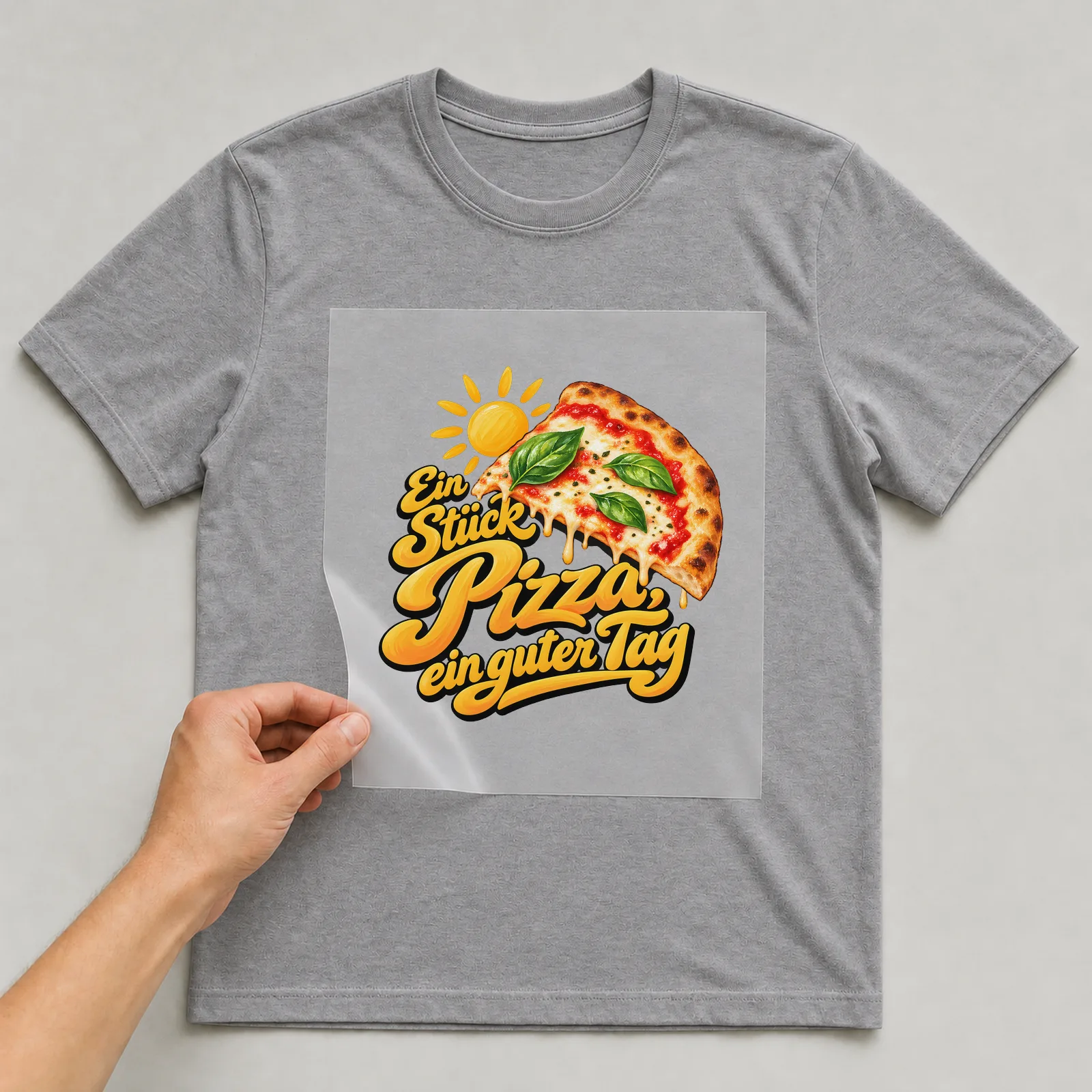 Bügelbild „Ein Stück Pizza, ein guter Tag“ auf grauem T-Shirt, Folie wird aufgelegt
