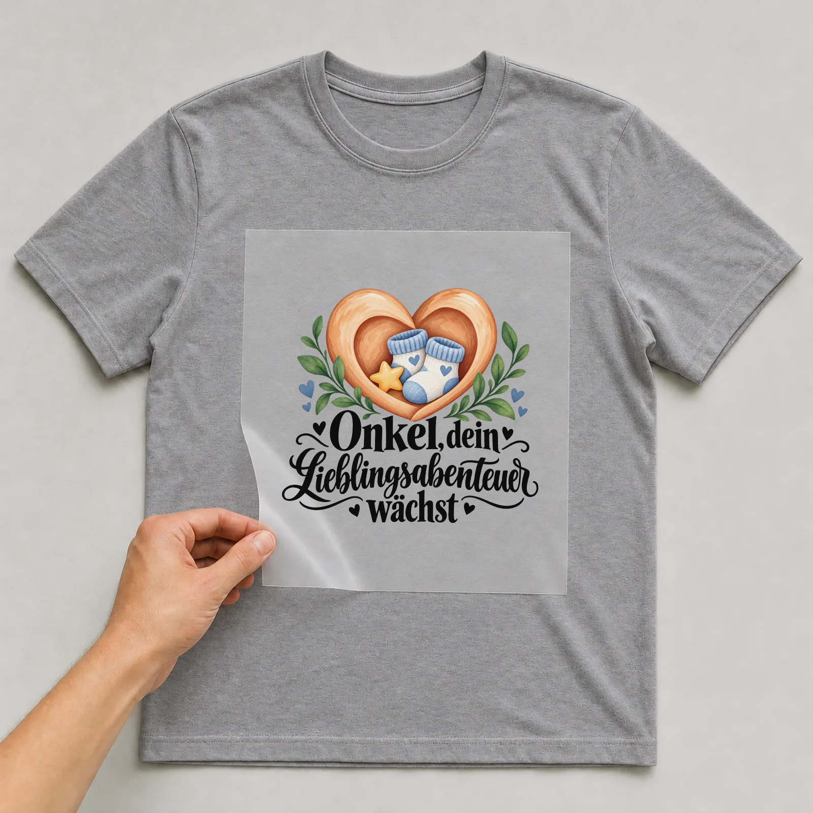 Bügelbild „Onkel, dein Lieblingsabenteuer wächst“ auf grauem T-Shirt, Folie wird aufgelegt