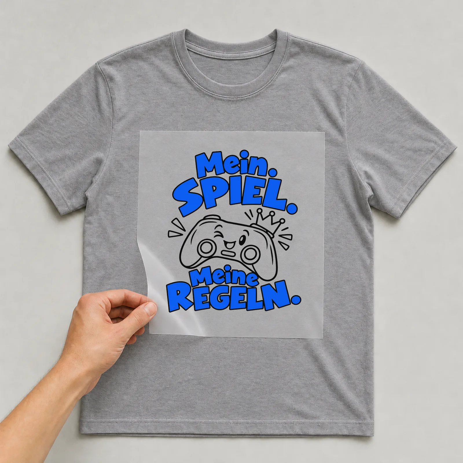 Bügelbild „Mein Spiel. Meine Regeln.“ auf grauem T-Shirt, Folie wird aufgelegt