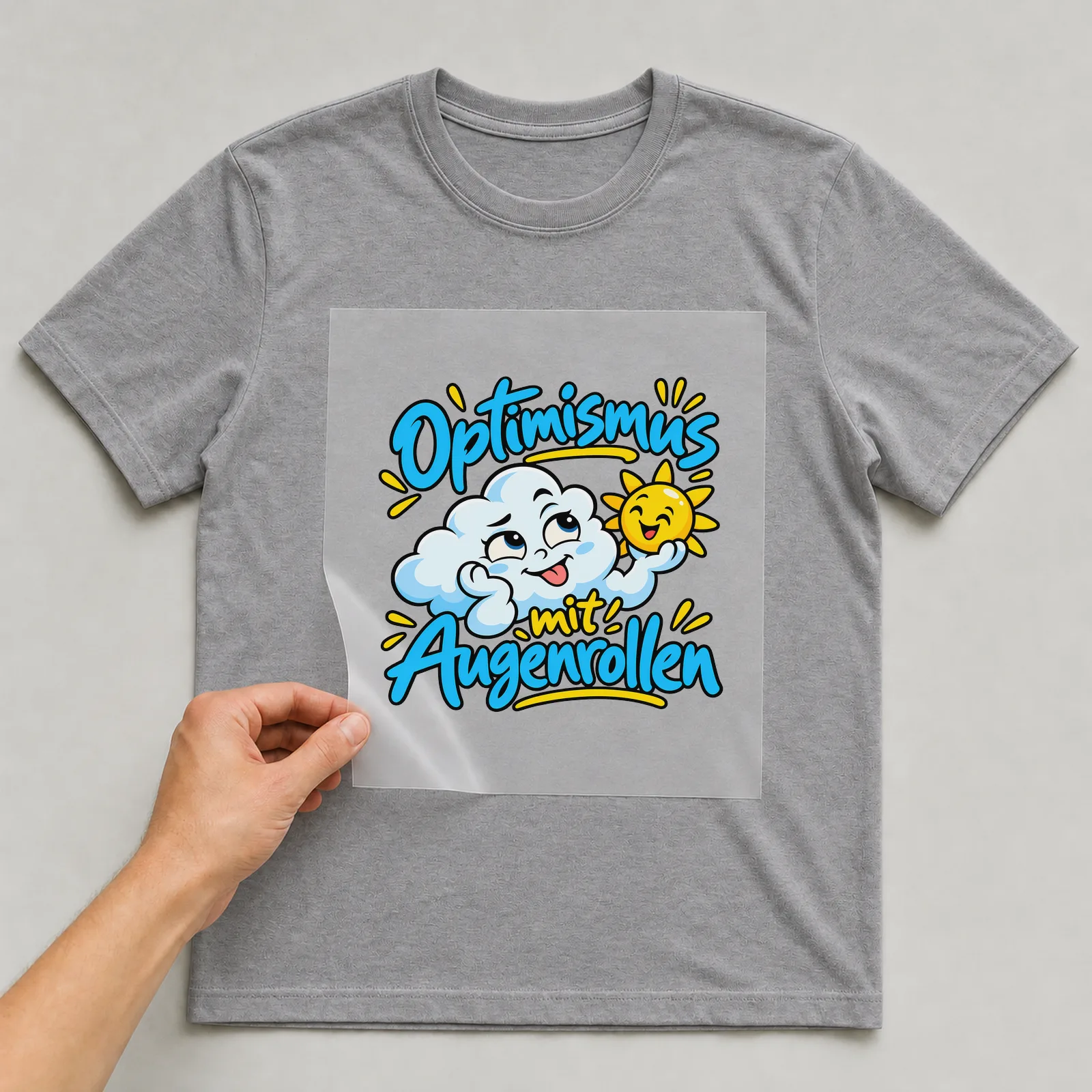 Bügelbild „Optimismus mit Augenrollen“ auf grauem T-Shirt, Folie wird aufgelegt