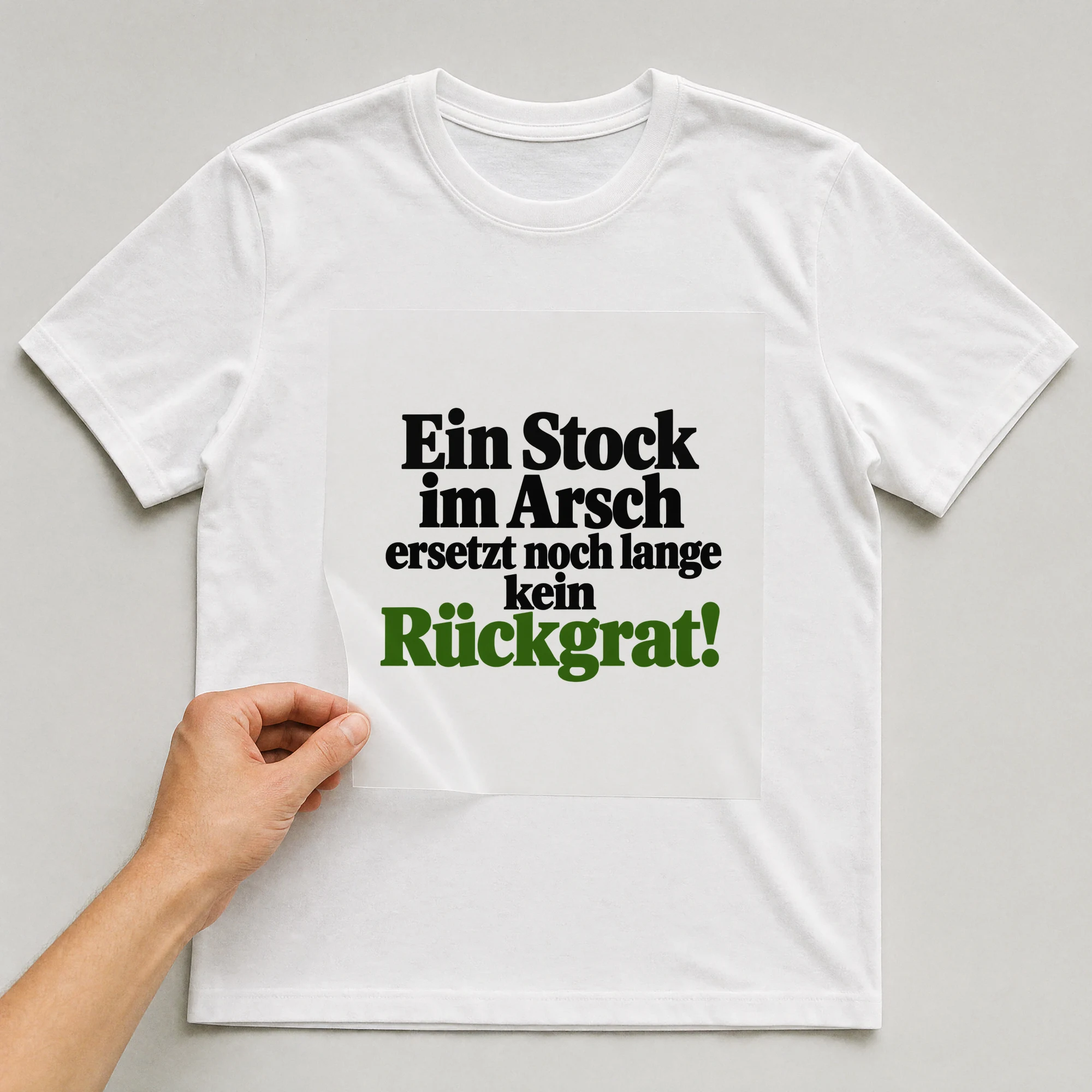 Bügelbild „Ein Stock im Ar**h ersetzt noch lange kein Rückgrat!“ auf weißem T-Shirt, Folie wird aufgelegt