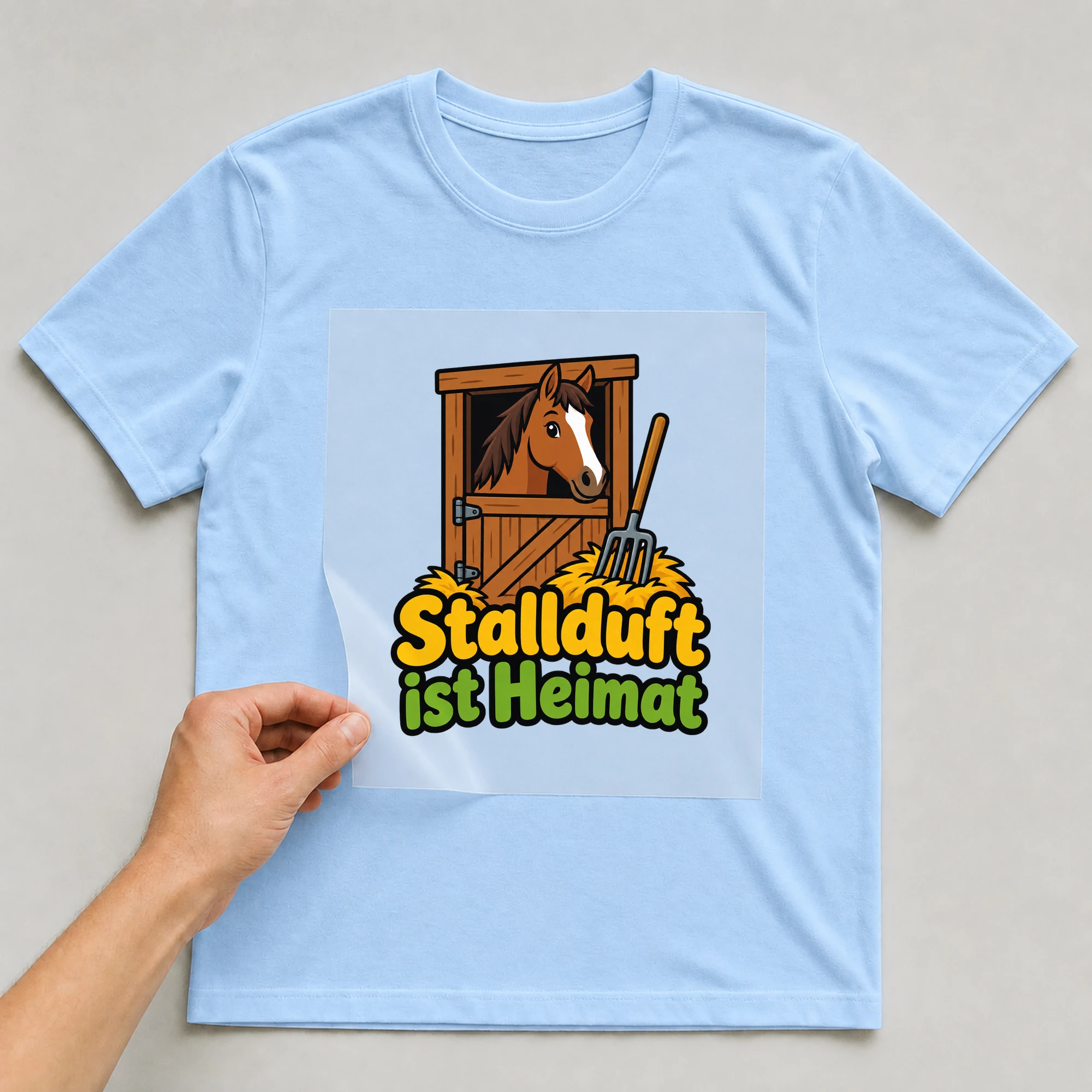 Bügelbild „Stallduft ist Heimat“ auf babyblauem T-Shirt, Folie wird aufgelegt