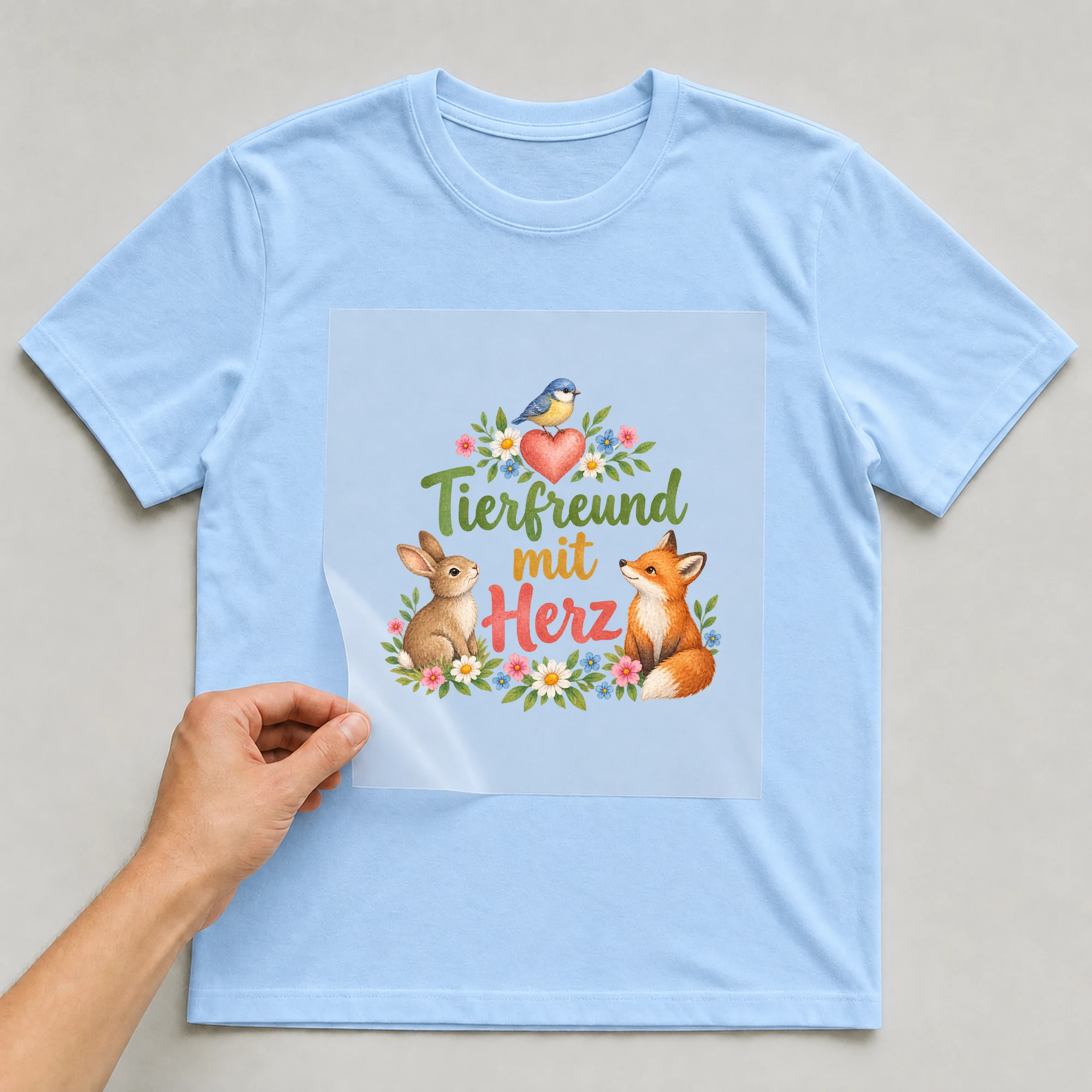 Bügelbild „Tierfreund mit Herz“ auf babyblauem T-Shirt, Folie wird aufgelegt